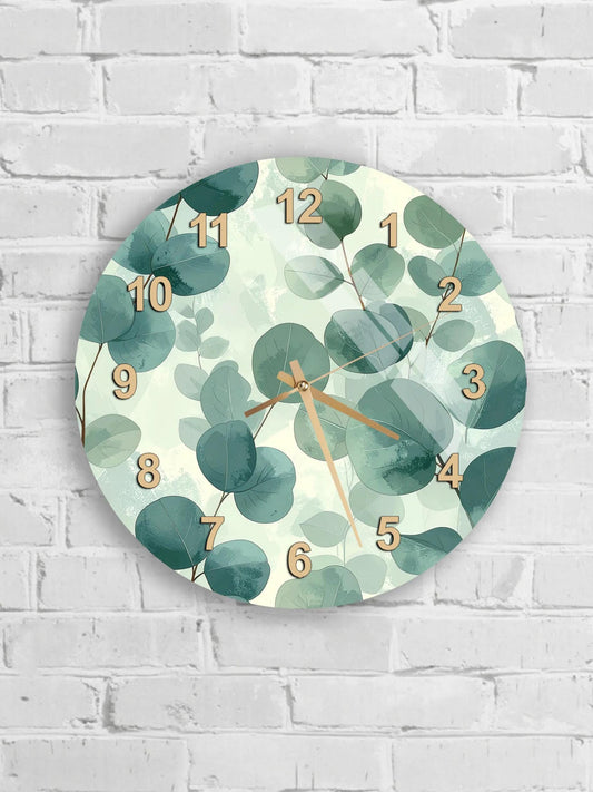 A round wall clock with a green leaf pattern and gold numbers is mounted on a white brick wall.