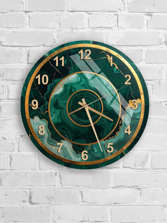 A wall clock with a green marble-like design and gold accents, mounted on a white brick wall.