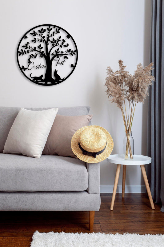 May include: Black metal wall art depicting a tree with leaves and birds. The tree has two cats sitting at the base. The text 'Custom Text' is written on the sign hanging from the tree.