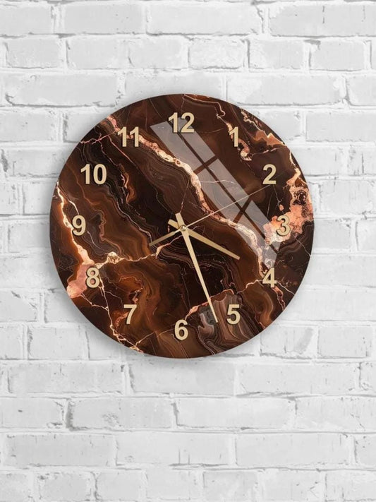 A round wall clock with a marble-like design and gold numbers is mounted on a white brick wall.