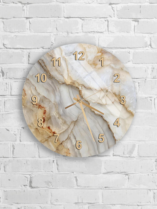 A round wall clock with a marble-like design and gold numbers is mounted on a white brick wall.
