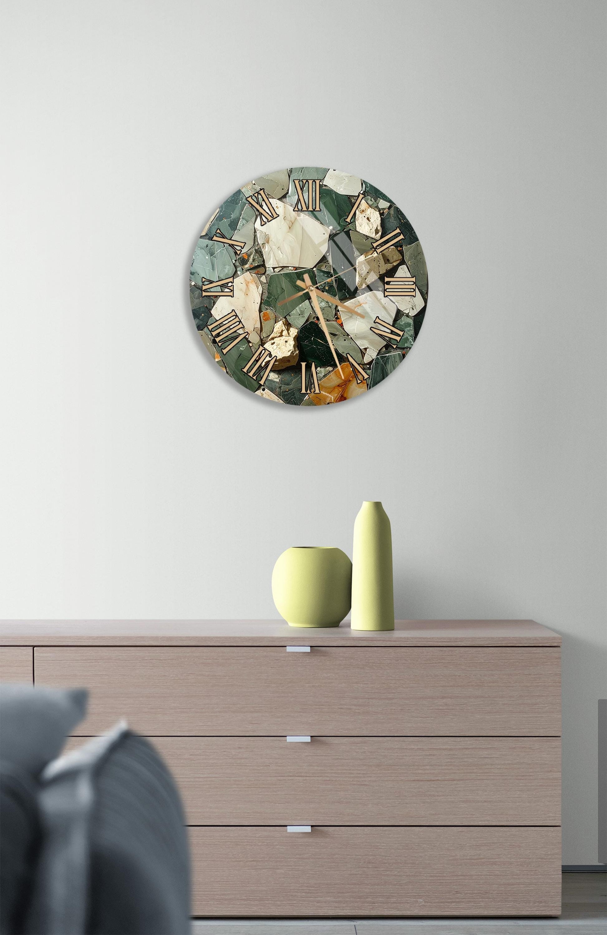 a modern clock with a mosaic design on the wall above a wooden dresser with three drawers. The dresser has a vase and a small sculpture on top of it.