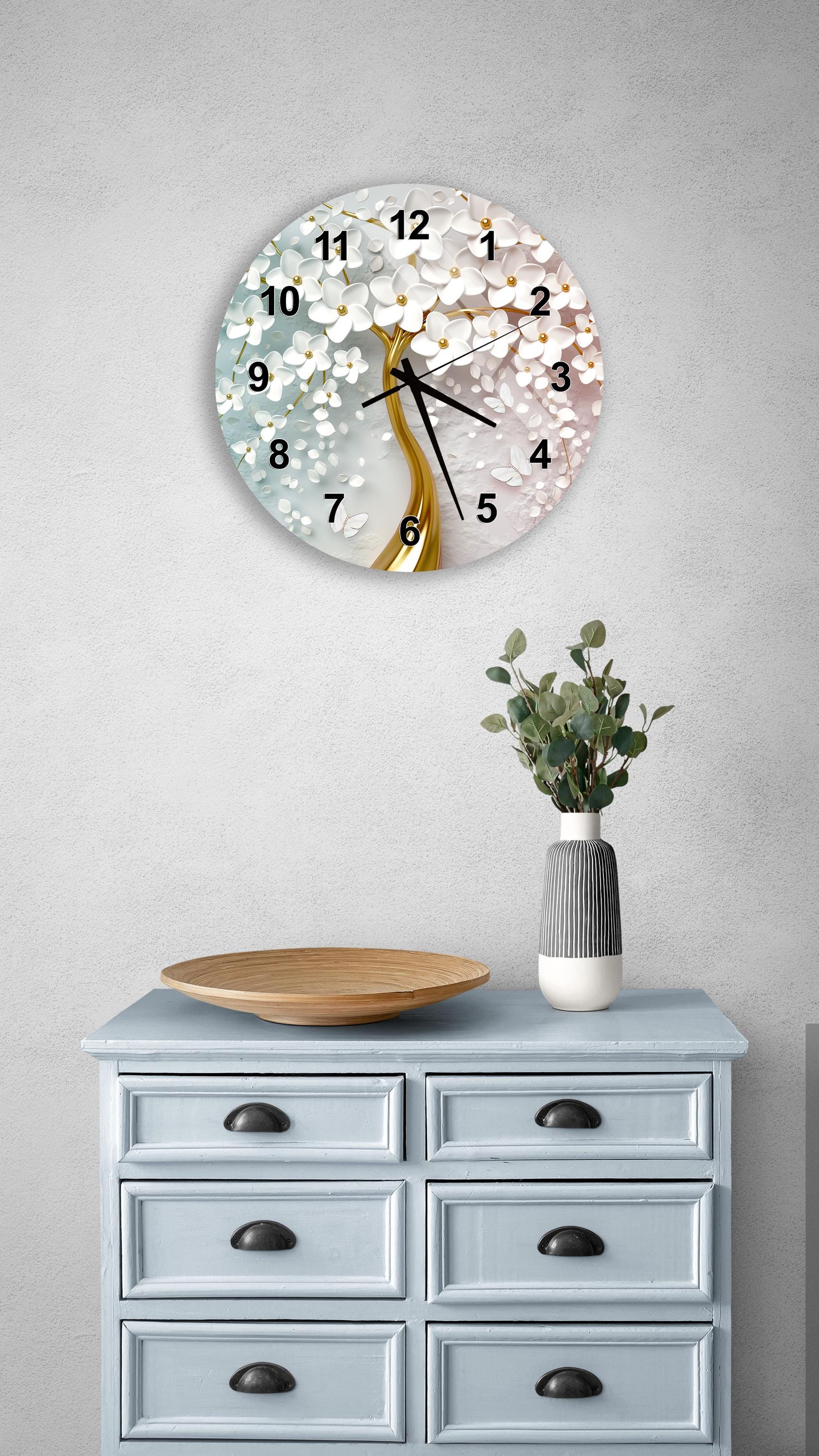 a wall clock with a tree design, a wooden bowl, and a vase with greenery on a light blue dresser.