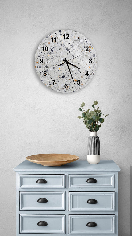 a wall clock with a speckled design, mounted on a wall above a light blue wooden dresser with six drawers. The dresser also has a vase with greenery on it, and a wooden plate on top.