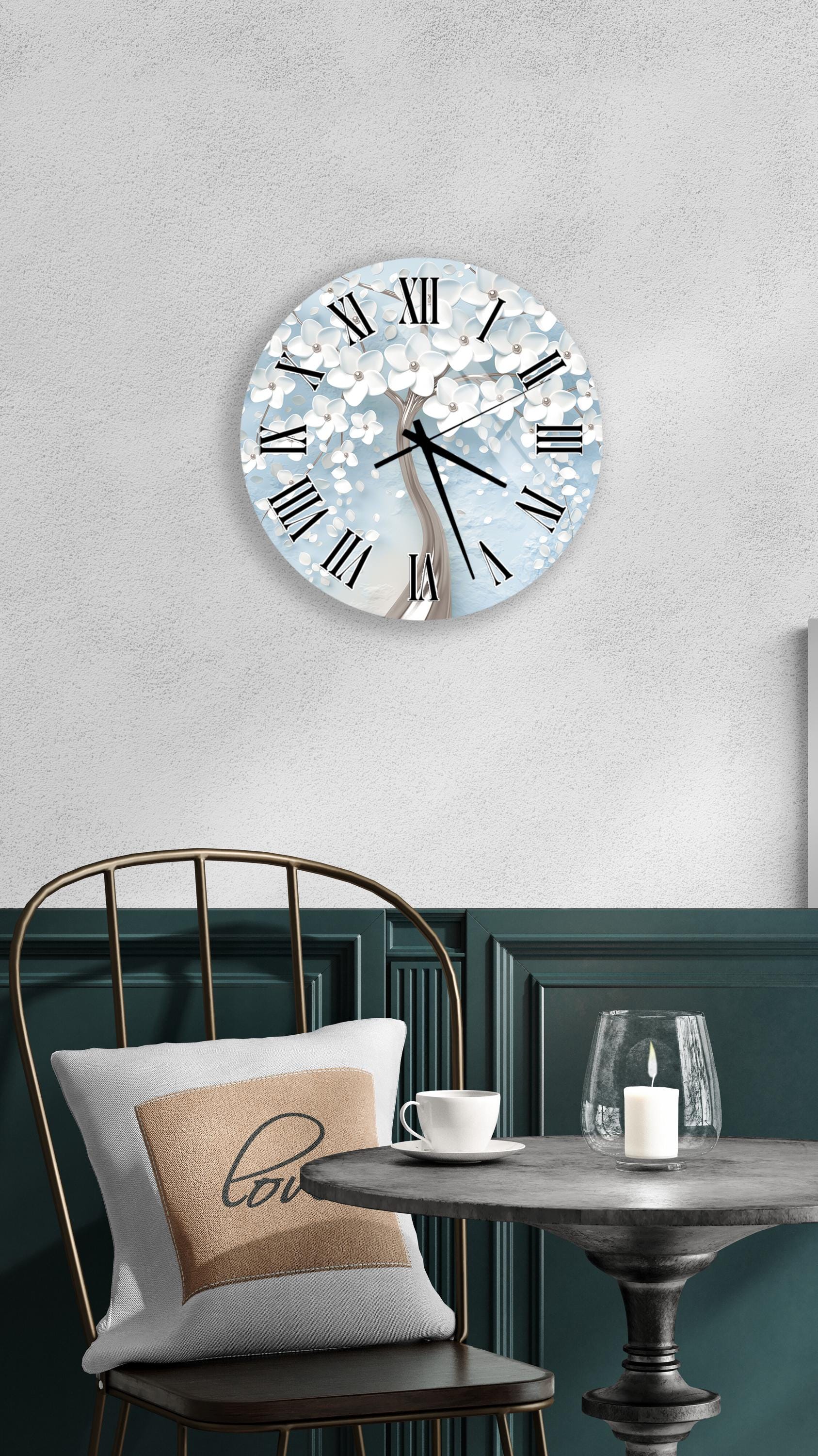 a cozy dining area with a round wall clock displaying a tree design, a white table with a candle and a cup, and a black chair with a pillow.