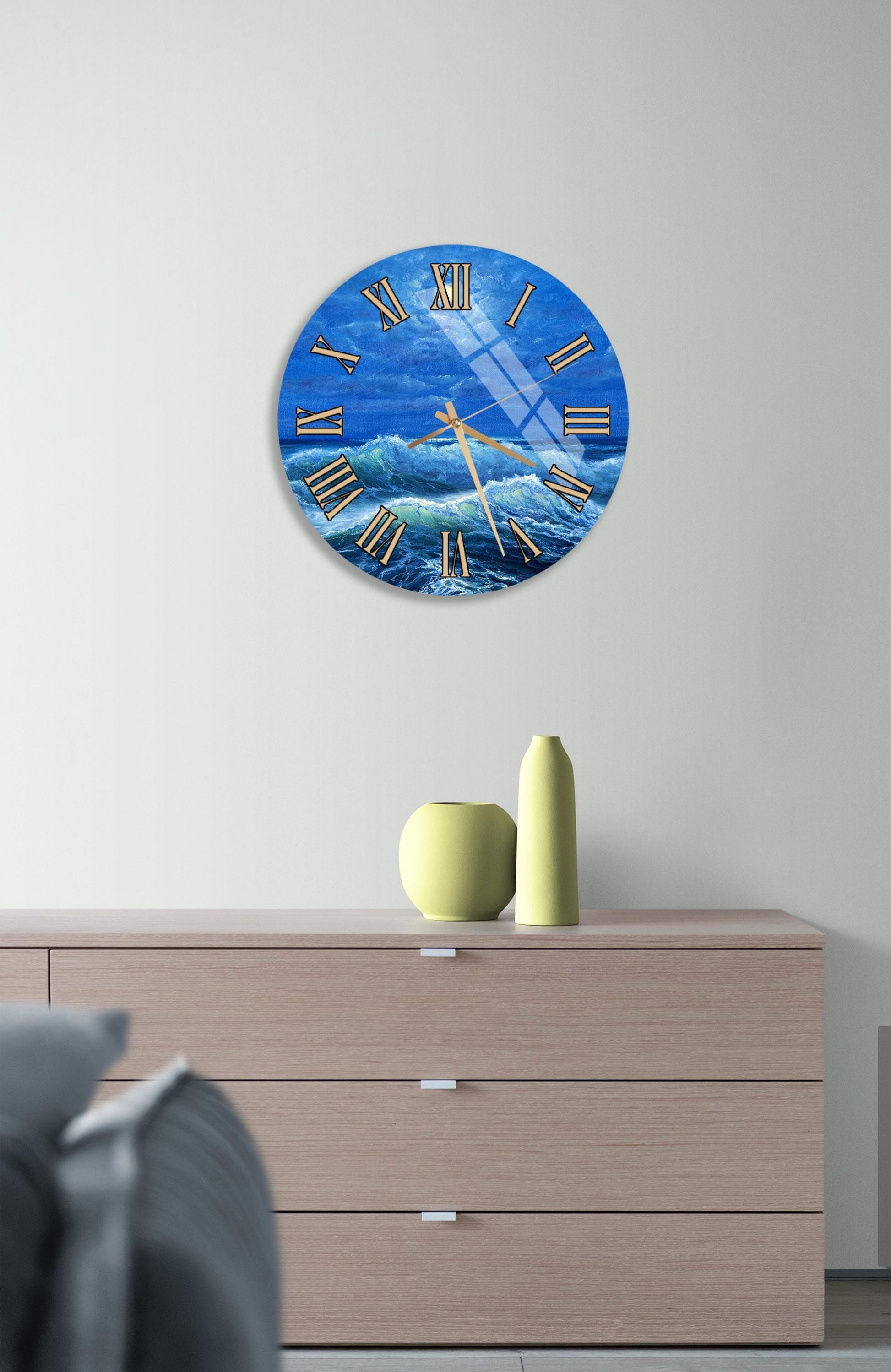 a wall clock with a blue ocean scene and a yellow vase on a wooden dresser.