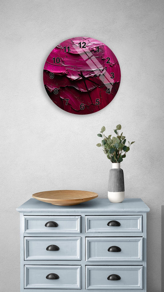 a round wall clock with a pink and purple design, mounted on a wall above a light blue dresser with six drawers. The dresser also has a wooden bowl and a vase with greenery on it.