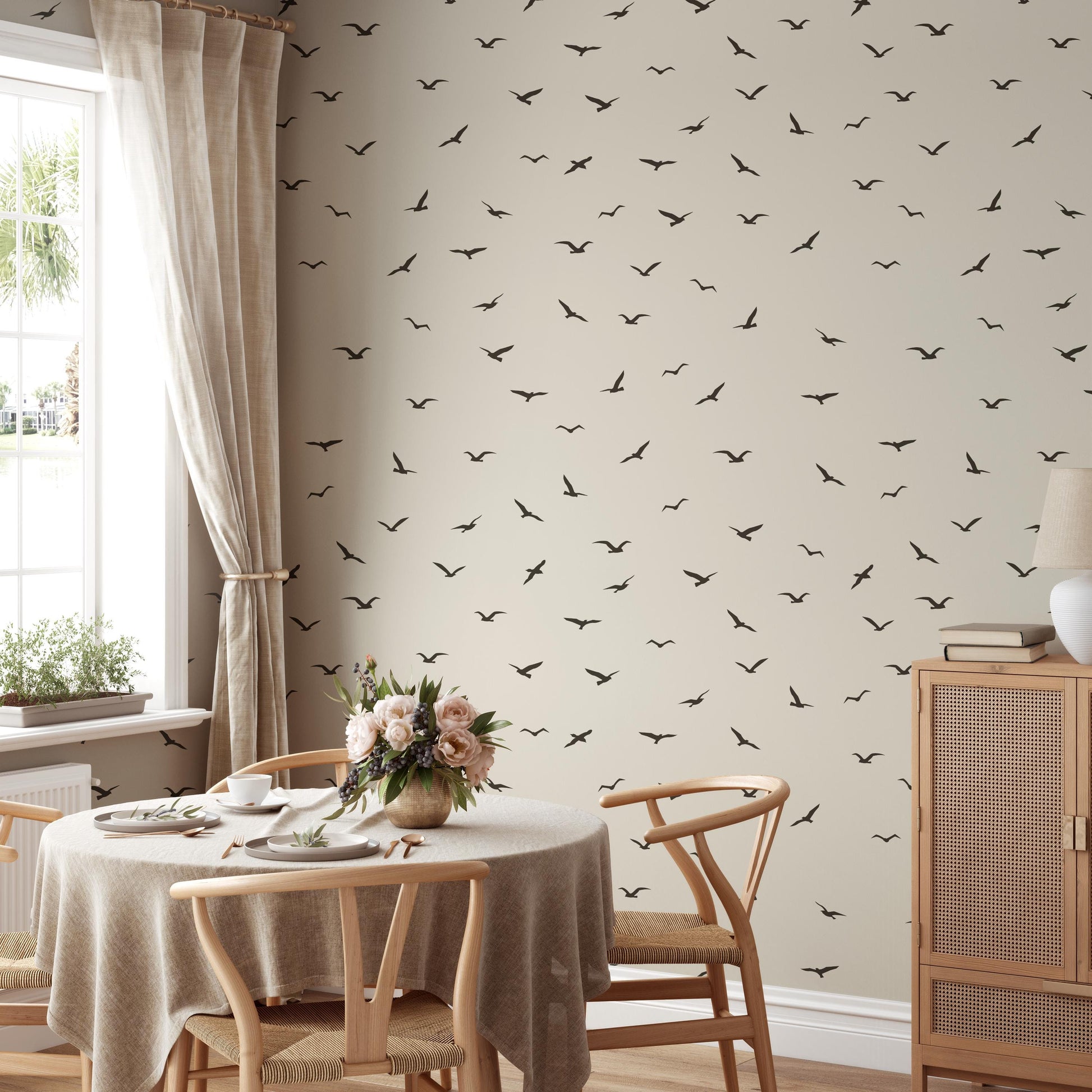 a dining room with a table set for two, featuring a vase of flowers and a bowl of fruit. The wall behind the table is covered in a pattern of black birds, creating a unique and eye-catching design element.