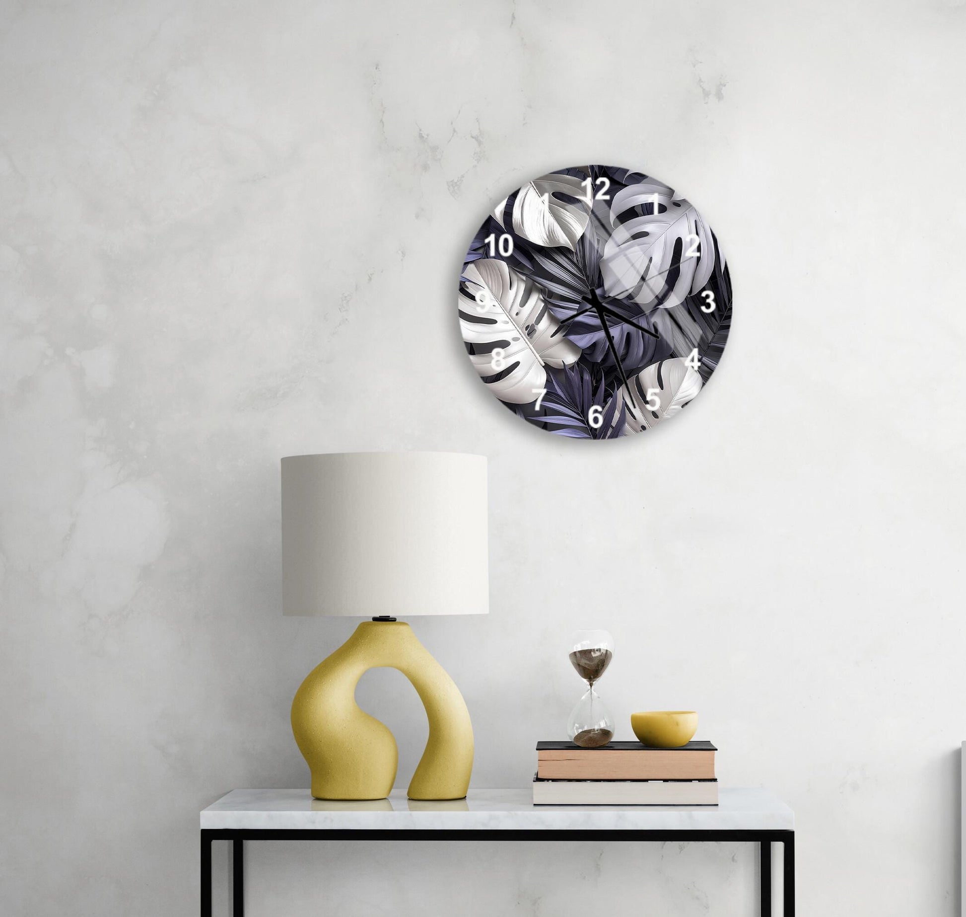 a modern living room with a white marble wall, a round clock with a black and white leaf pattern, a yellow lamp with a unique curved base, a stack of books, and a glass of wine on a white table.