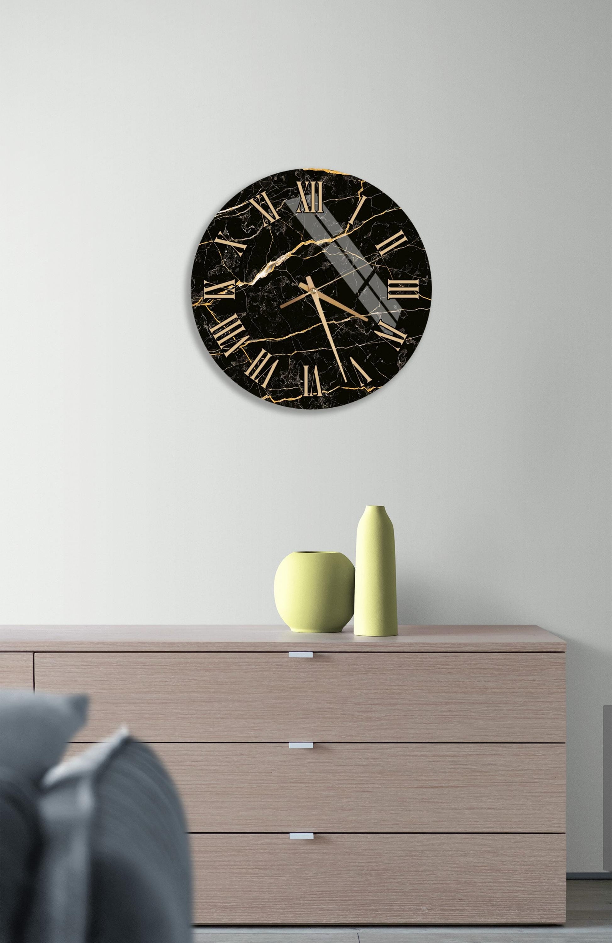 a modern black and gold clock mounted on a white wall above a wooden dresser with three drawers.