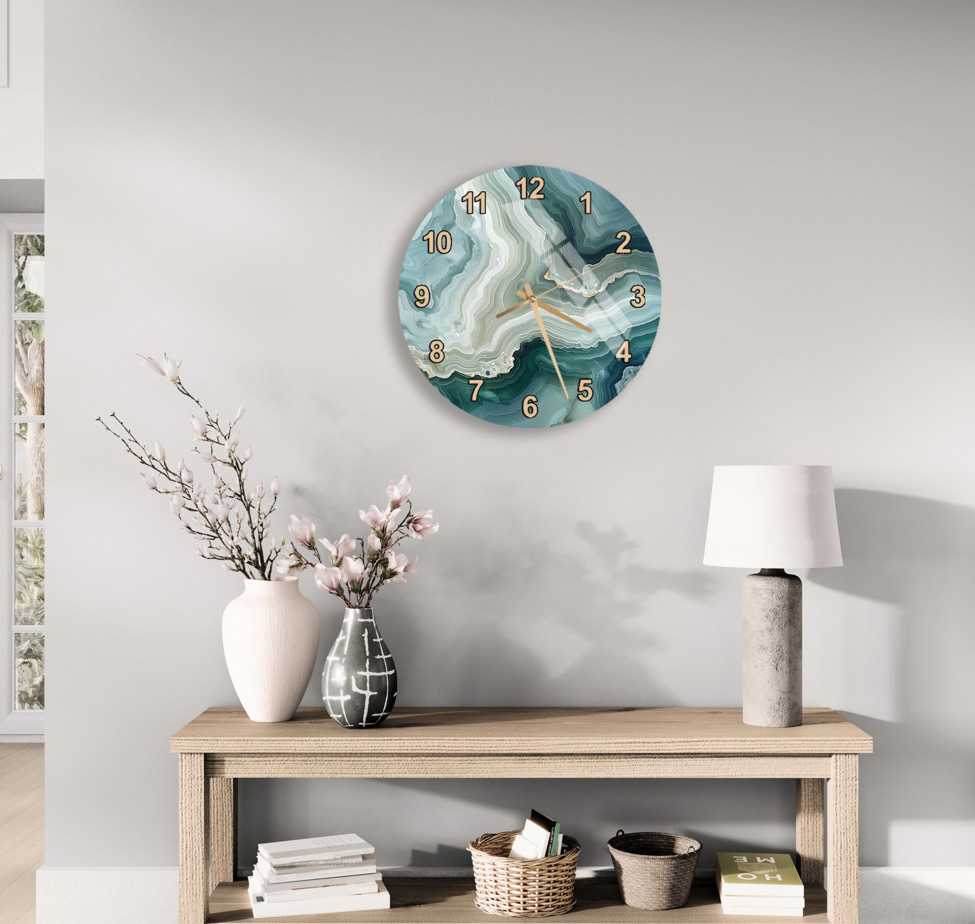 a modern living room with a wooden console table, a round wall clock with a marble-like design, a lamp, a vase with pink flowers, and a stack of books.