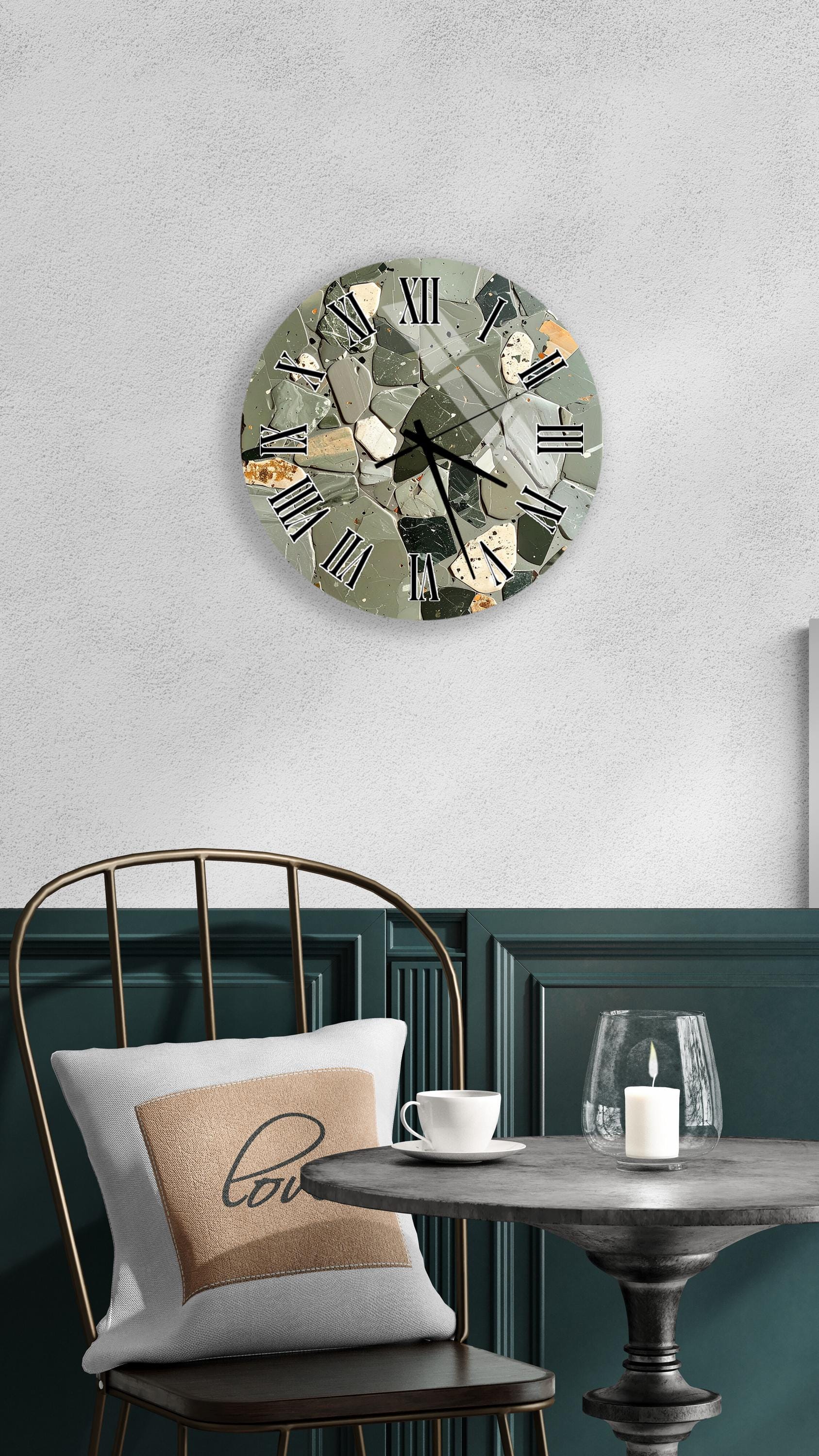 a modern, round clock with a mosaic design on its face, mounted on a wall above a table with a white tablecloth. The table is set with a white cup and a candle, creating a cozy and inviting atmosphere.
