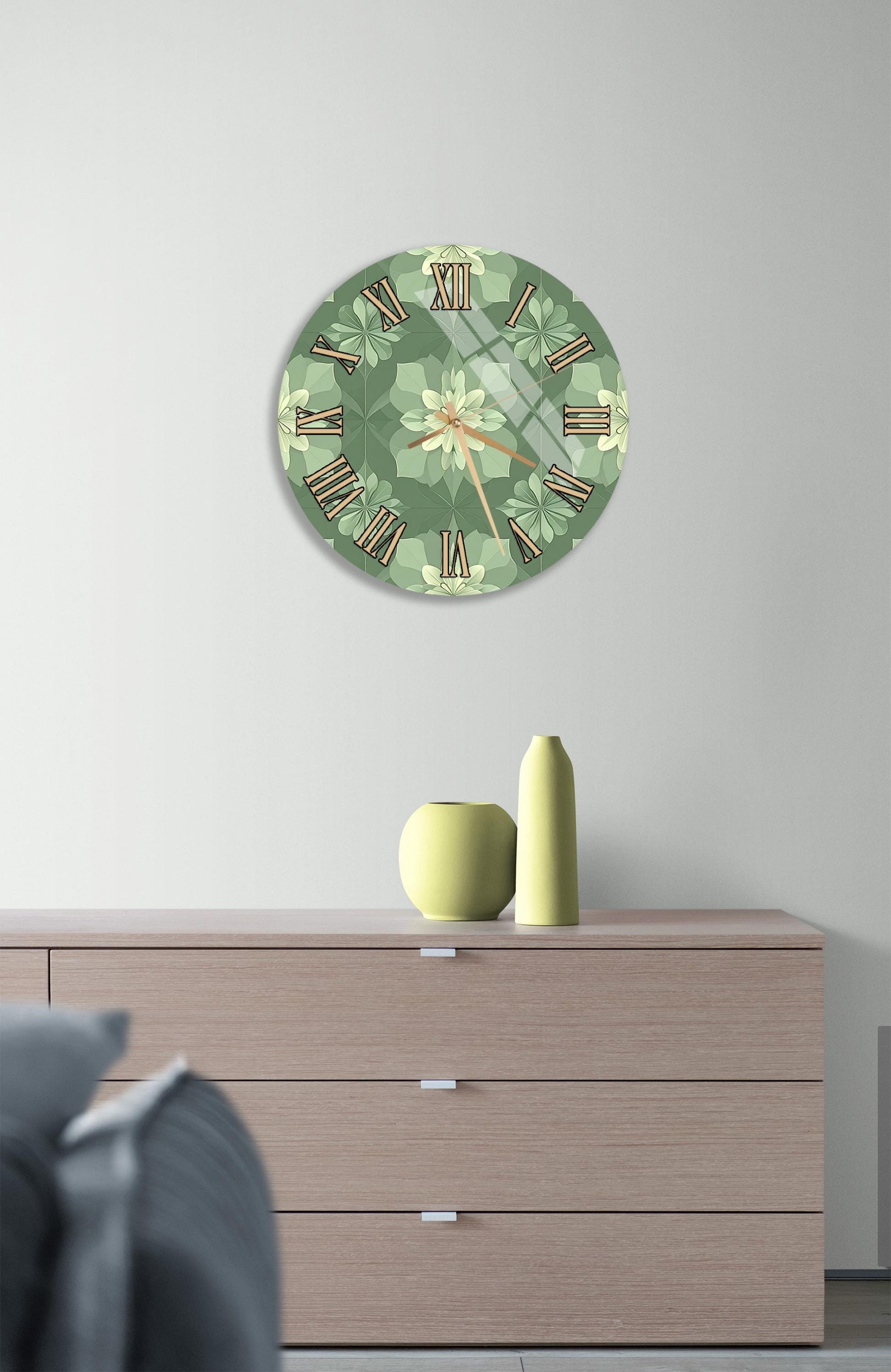 a wall clock with a green floral design, mounted on a wall above a wooden dresser with three drawers.