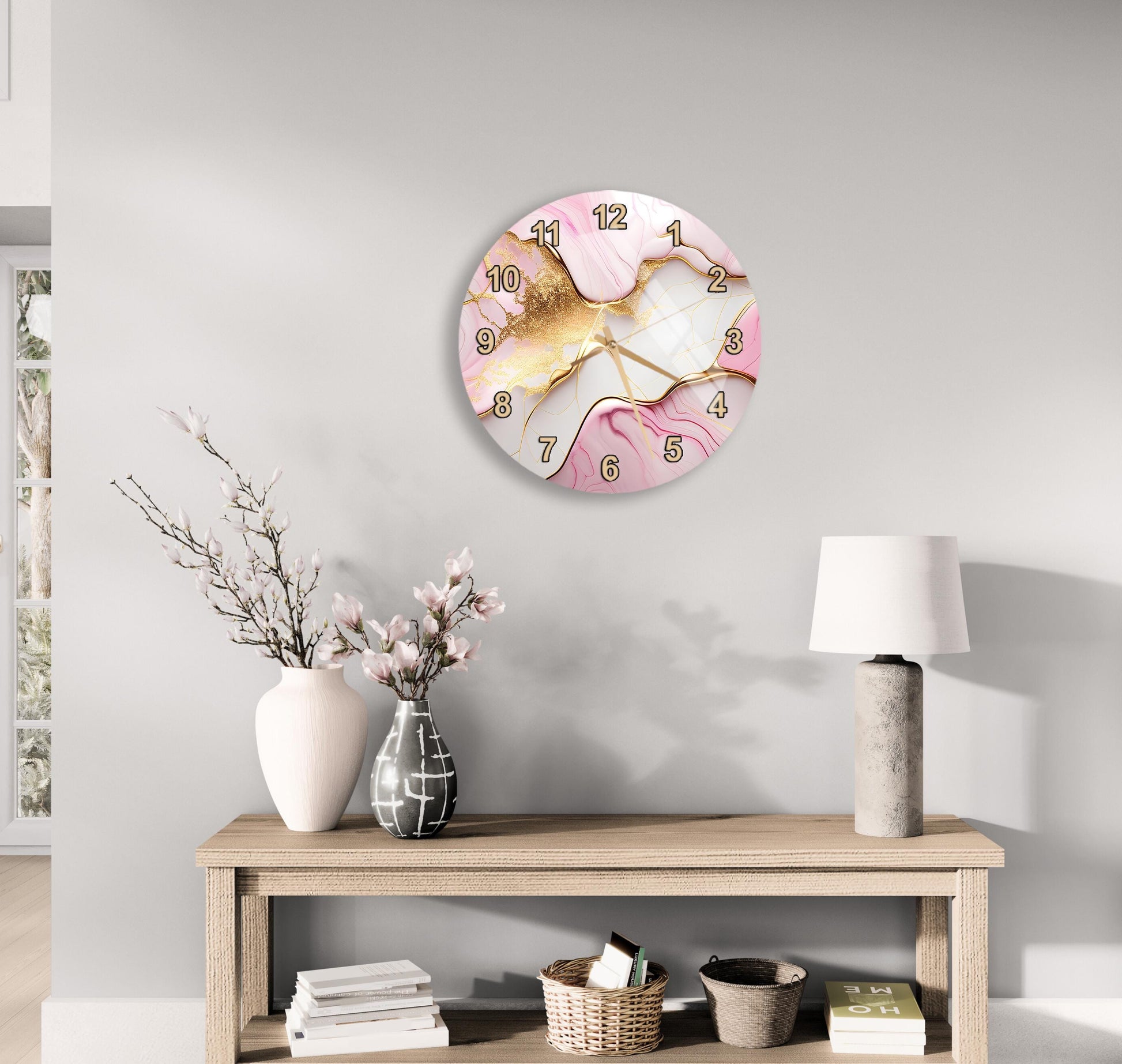 a wall clock with a pink and gold marble design, a wooden table with a lamp, a vase with flowers, and some books on a shelf.