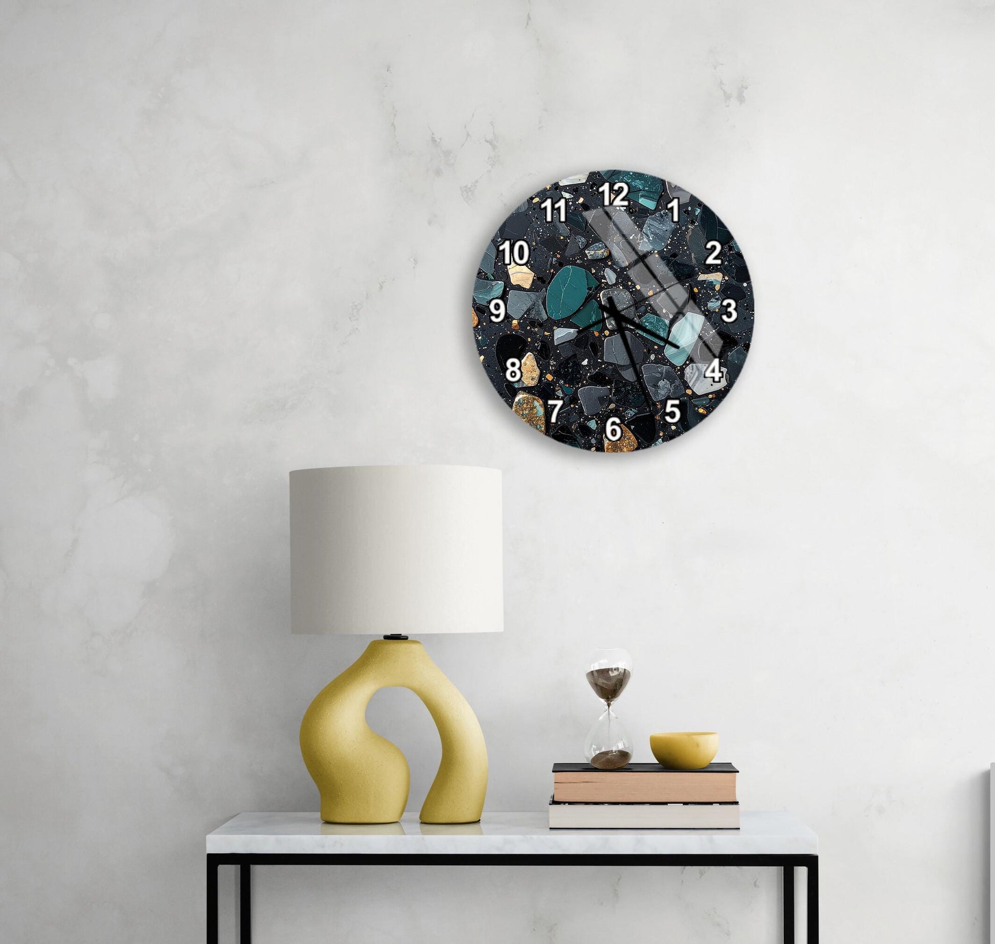 a modern clock with a black and blue design, mounted on a white wall above a white table with a yellow lamp and a stack of books.