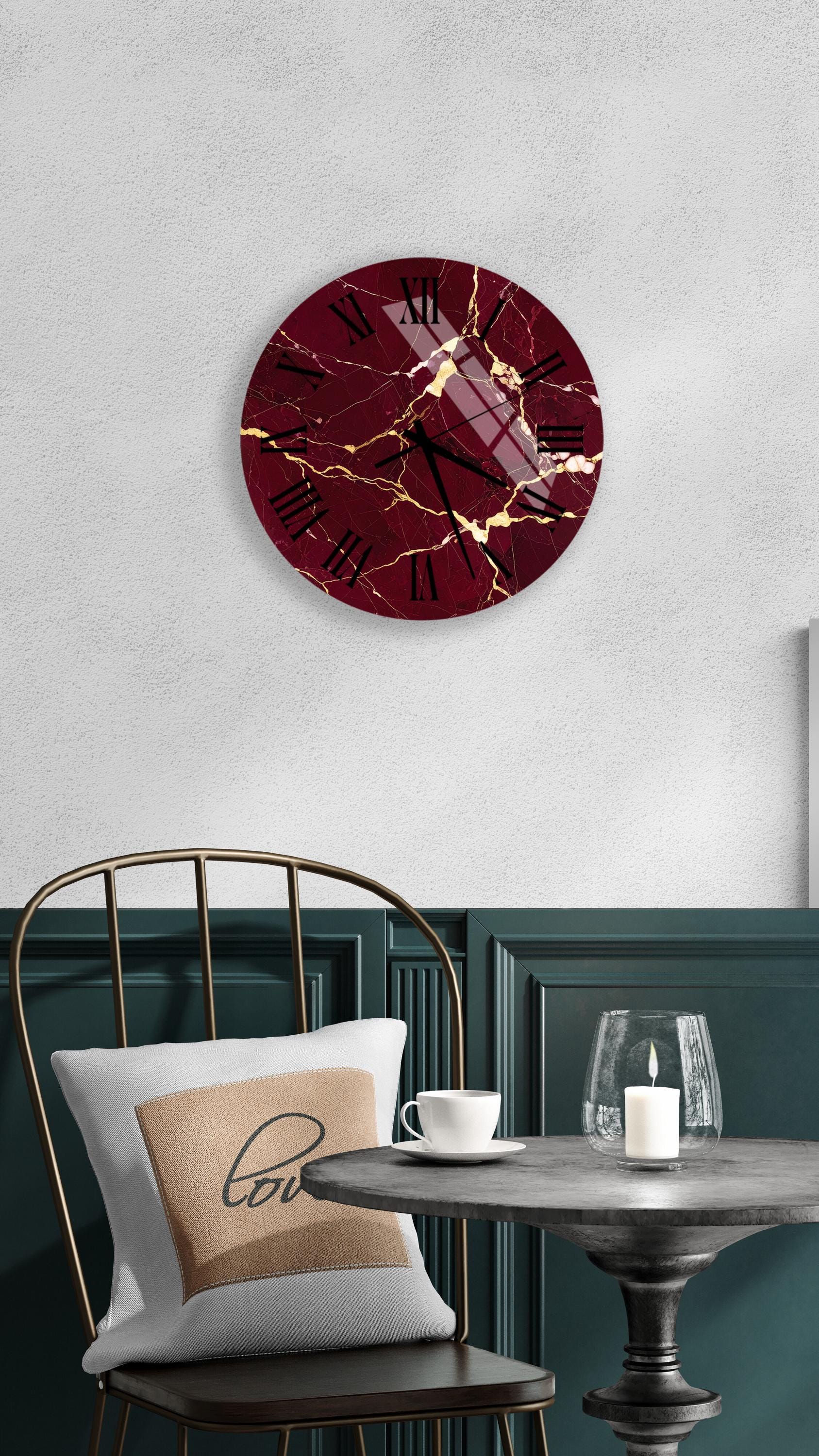 a modern interior design with a maroon-colored clock with a cracked and gold-colored face, a white table with a candle and a cup, and a black metal chair with a white pillow.