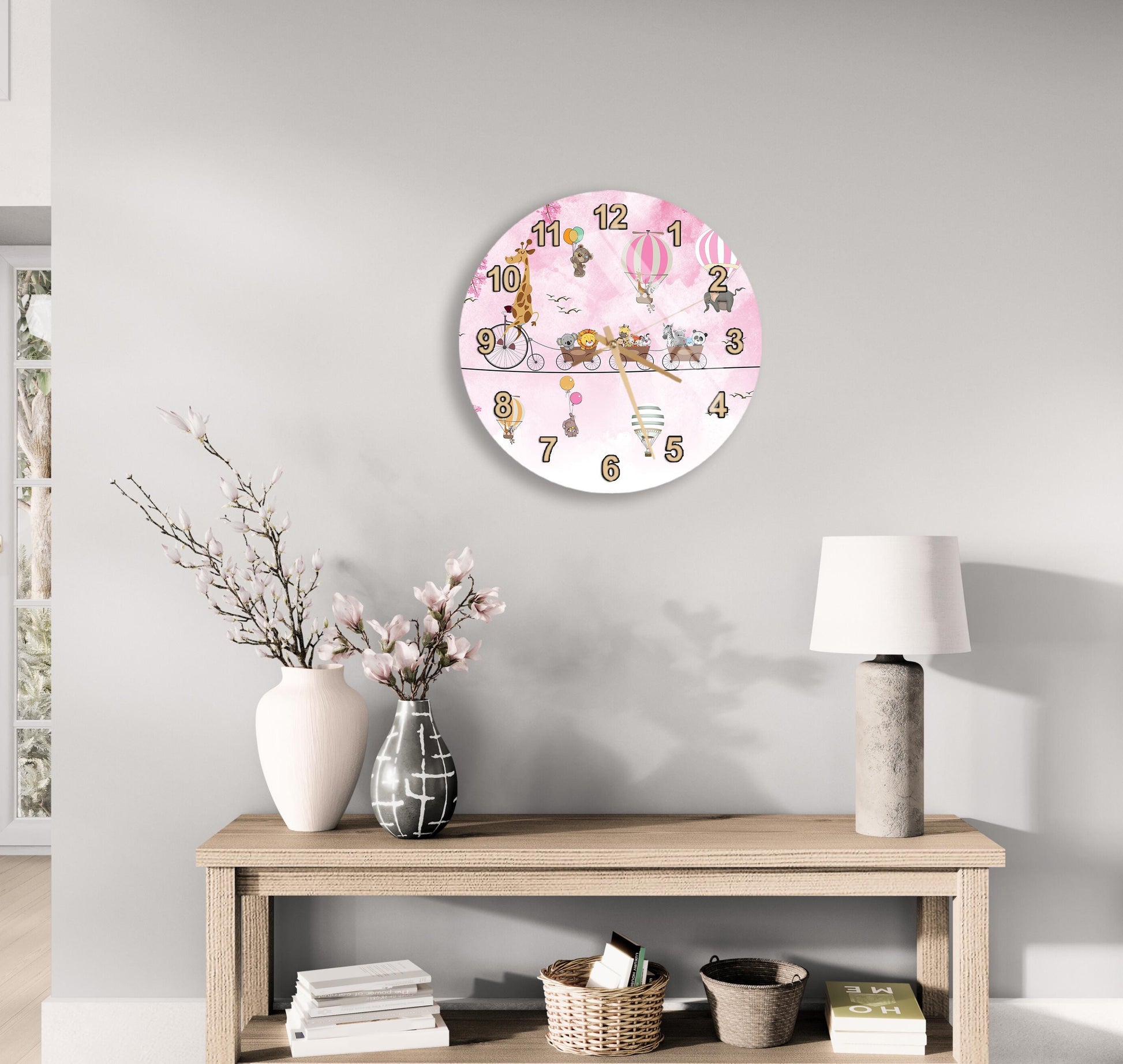 a wall clock with a pink and white design, a wooden table with a lamp, a vase with flowers, and some books on a shelf.