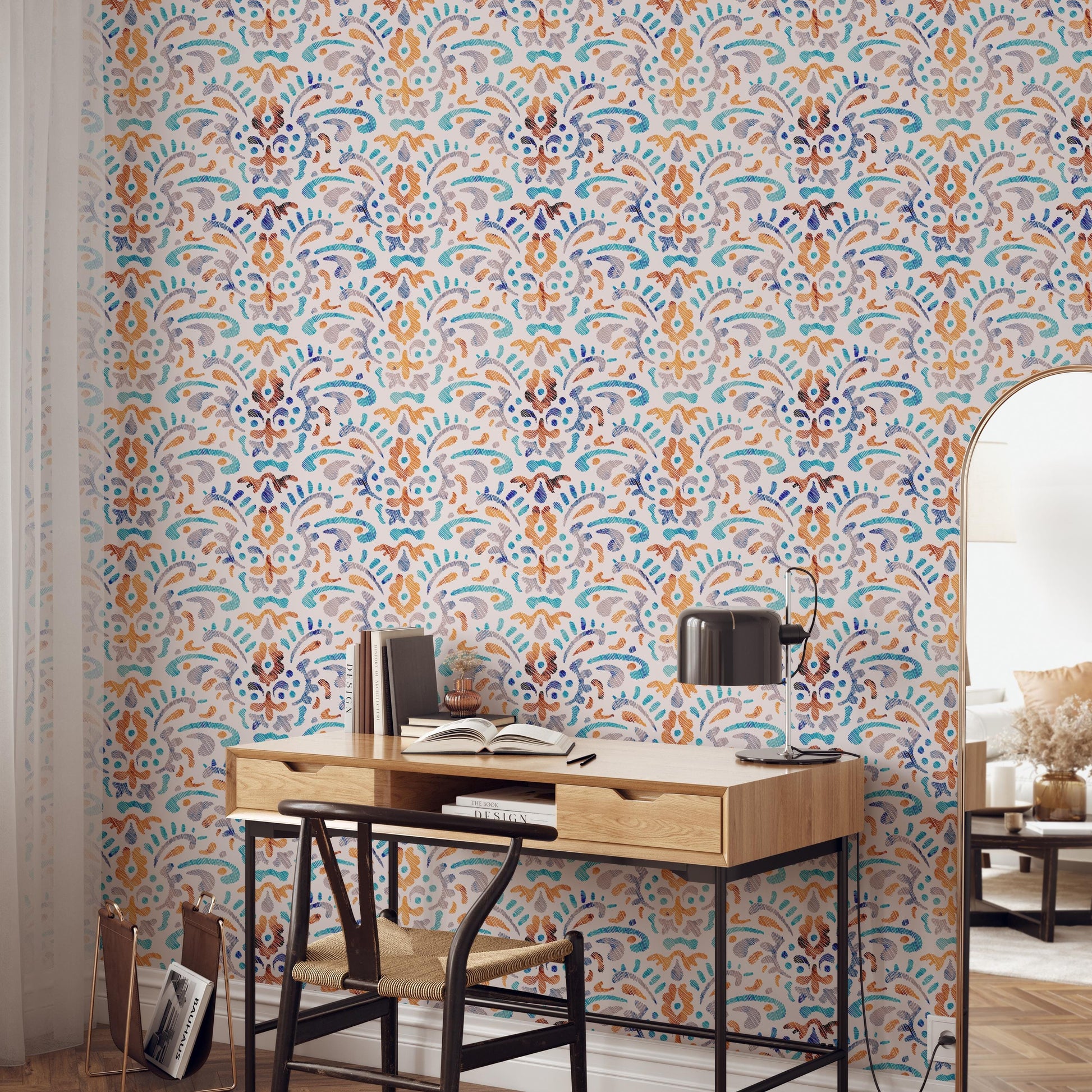 a modern and stylish workspace with a wooden desk, a black chair, and a lamp. The desk is positioned against a wall with a colorful, patterned wallpaper. There are several books and decorative items on the desk, suggesting a well-organized and functional workspace.