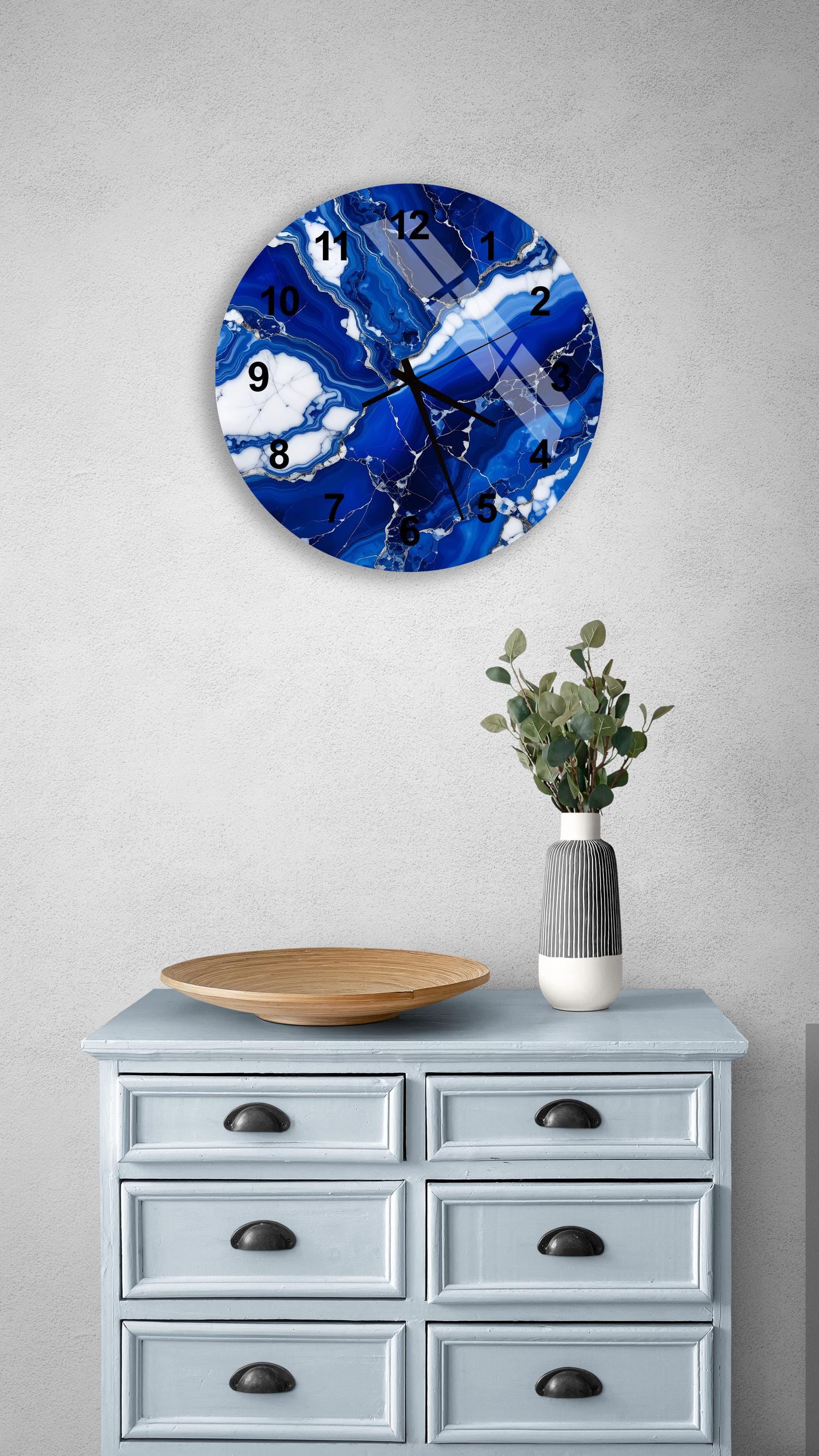 a blue and white marble clock mounted on a wall above a light blue dresser with six drawers. The clock has a marble-like design and displays the time. The dresser also has a vase with greenery on it, and there is a wooden bowl on top of it.