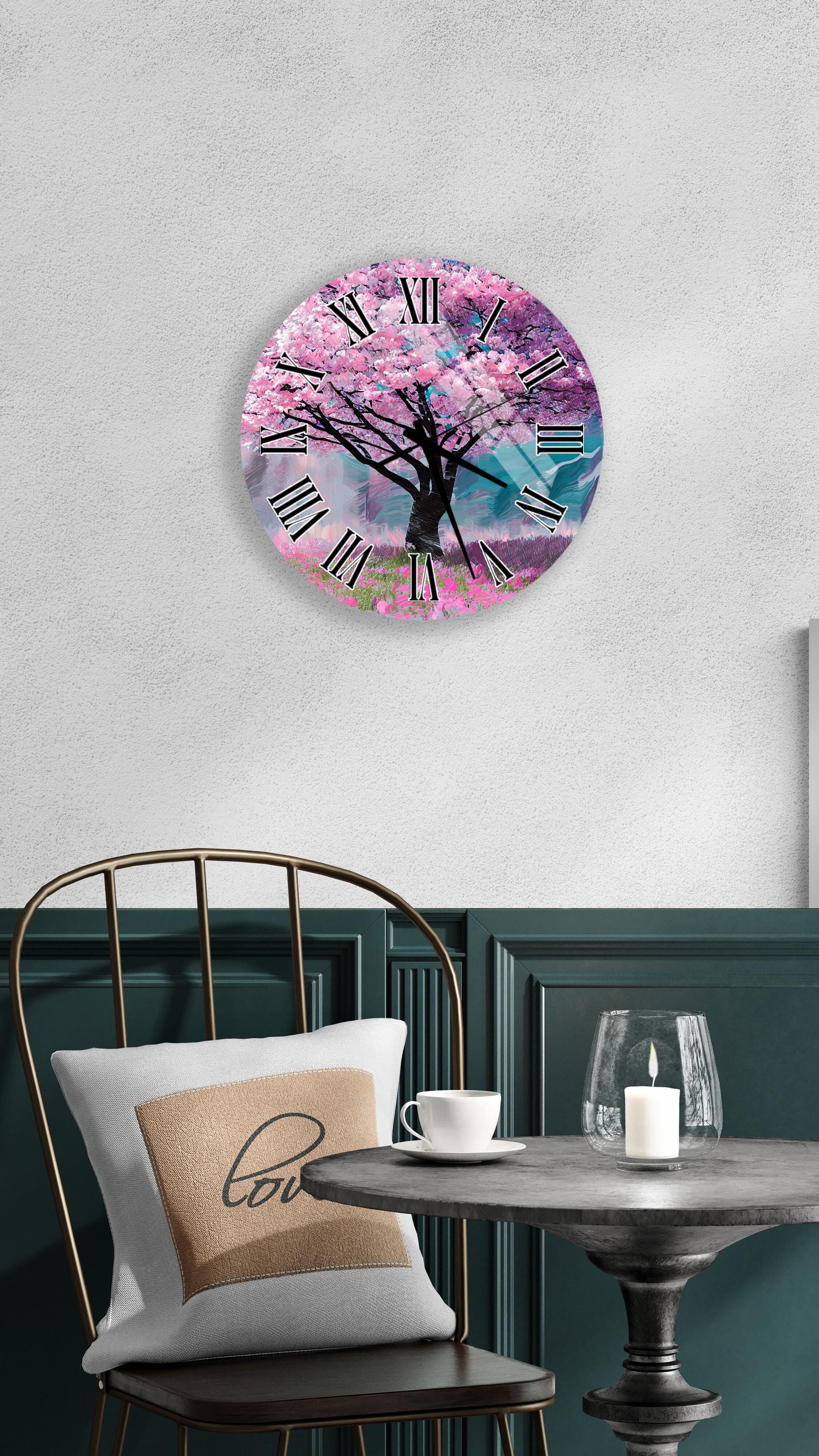 a round wall clock with a pink tree design, mounted on a wall above a table with a white tablecloth.