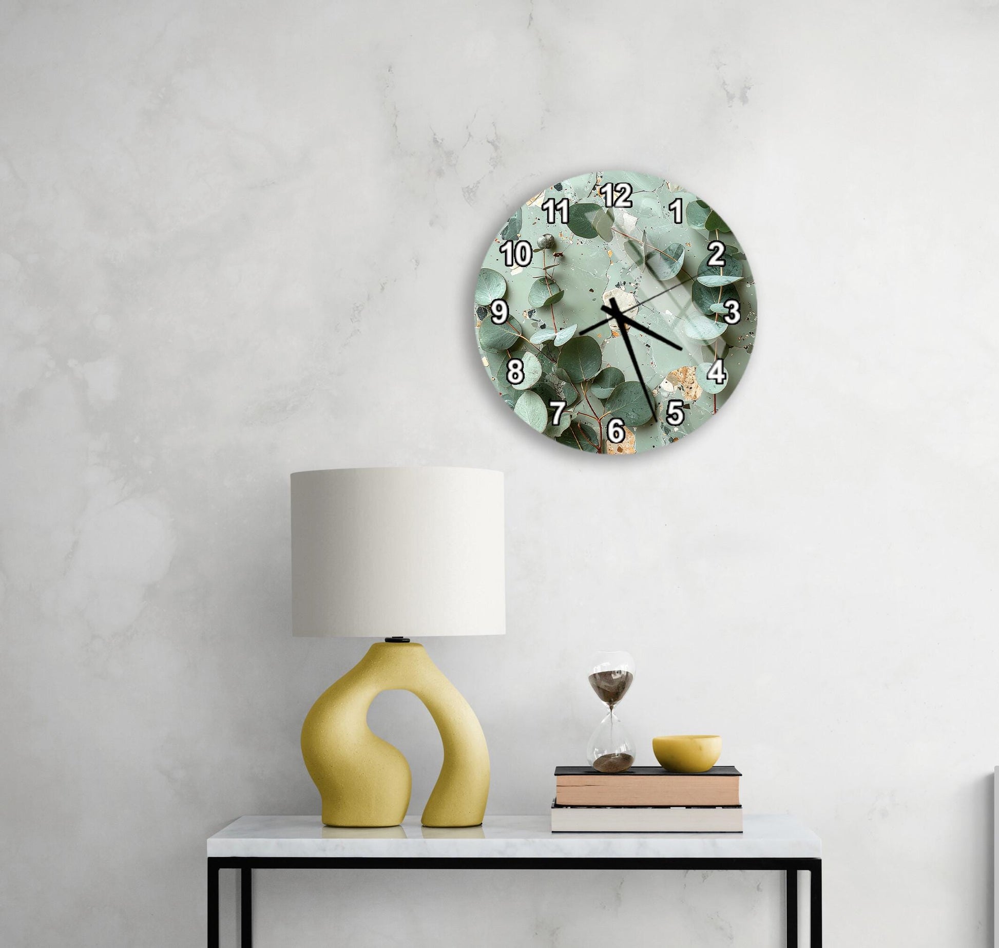 a modern living room with a round wall clock displaying a green floral pattern, a yellow lamp with a unique curved base, a stack of books, and a glass of wine on a white table.