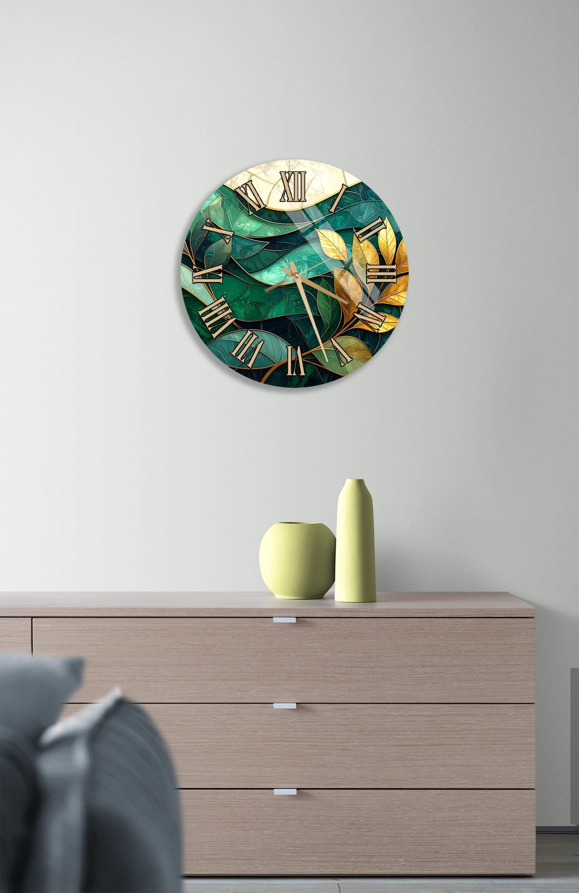 a round clock with a green and gold design, mounted on a wall above a wooden dresser with three drawers.