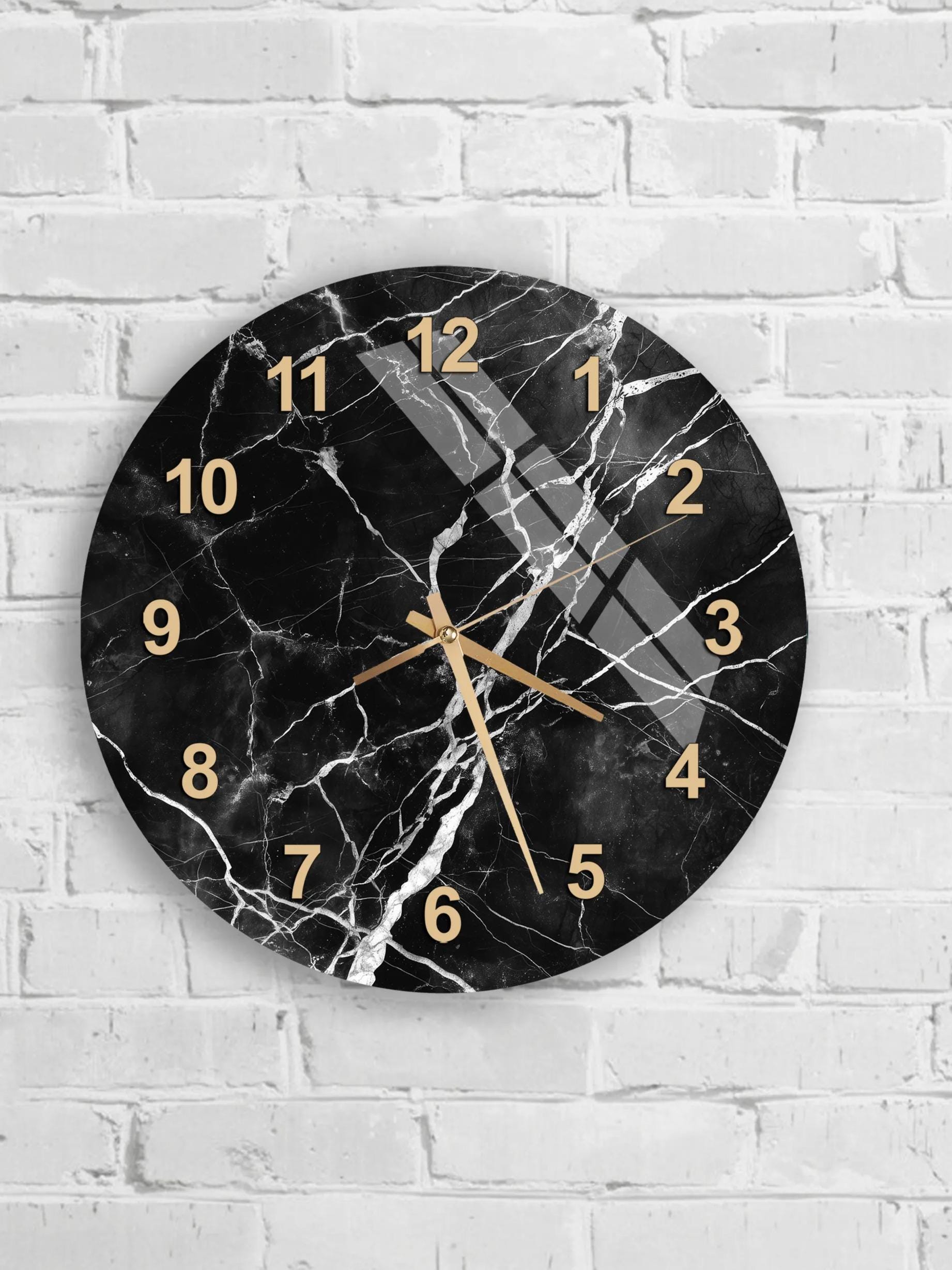 A black and white marble wall clock with gold hands and numbers is mounted on a white brick wall.