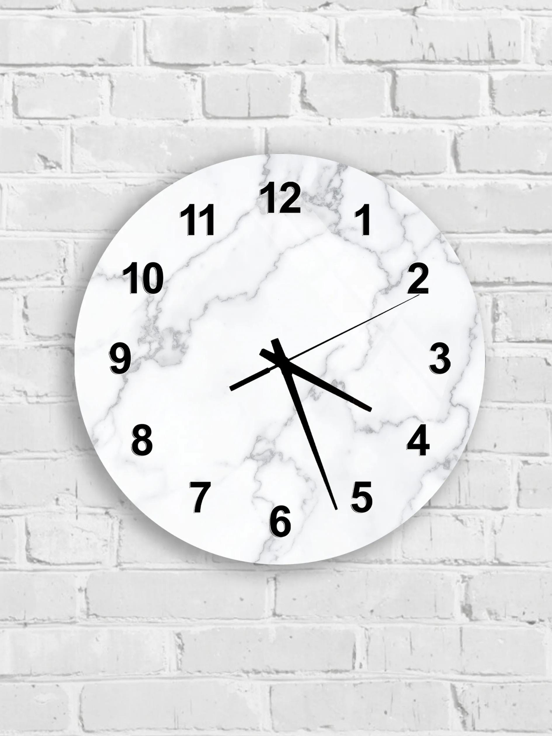 A white marble wall clock with black numbers and hands is mounted on a white brick wall.