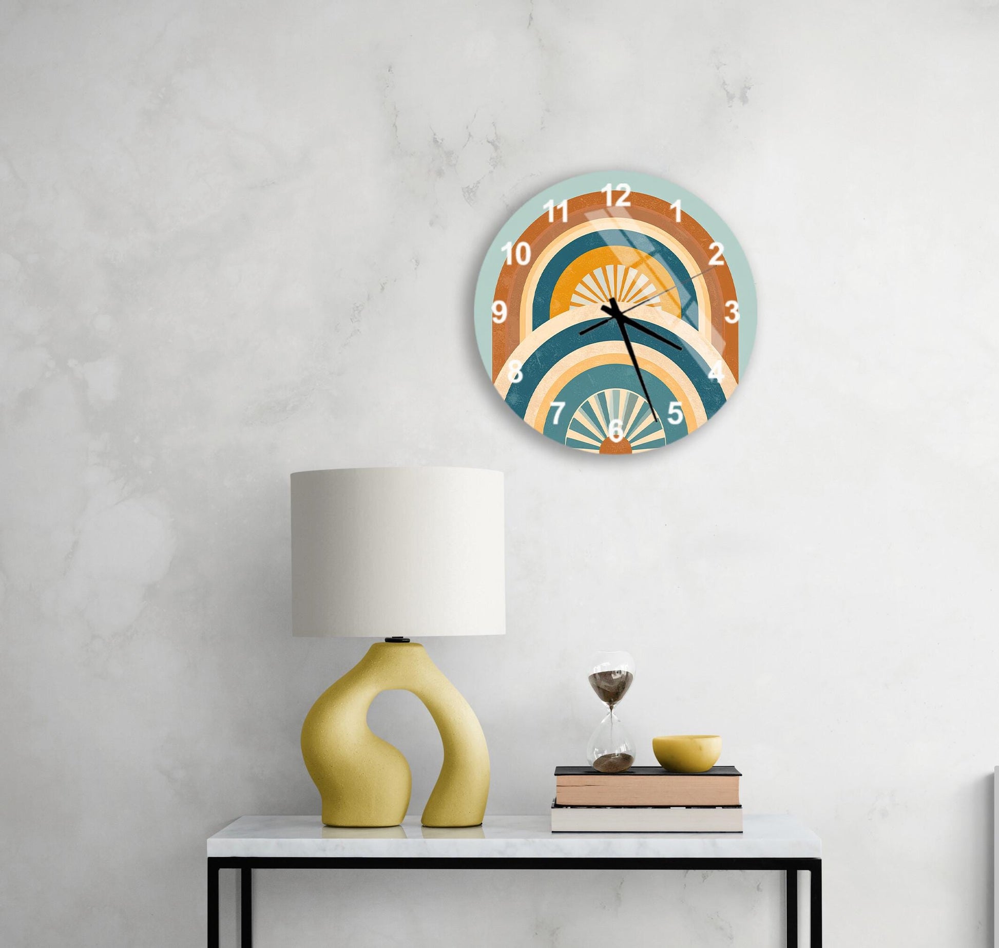a modern, abstract clock with a colorful design hanging on a white wall above a white table with a yellow lamp and a stack of books.