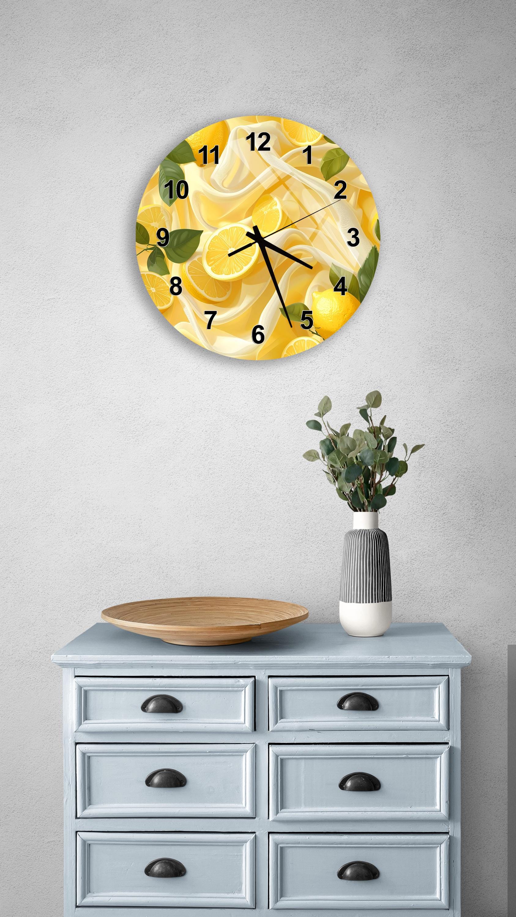 a wall clock with a yellow and green design, mounted on a wall above a light blue dresser with six drawers. The dresser also has a vase with greenery and a wooden tray on top.
