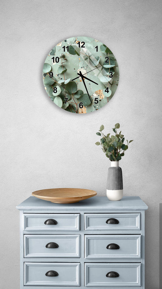 a wall clock with a green leaf design, a wooden bowl on a light blue dresser, and a vase with greenery on a gray wall.