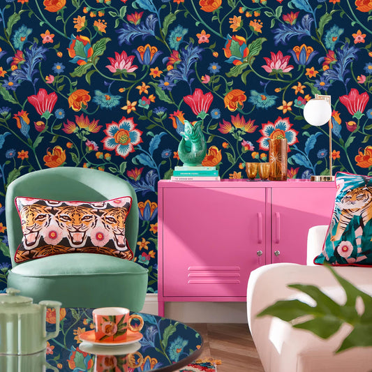 a vibrant and eclectic living room with a bold floral wallpaper, a pink cabinet, a green armchair, a glass coffee table, and various decorative elements such as a vase, a lamp, and a plant.