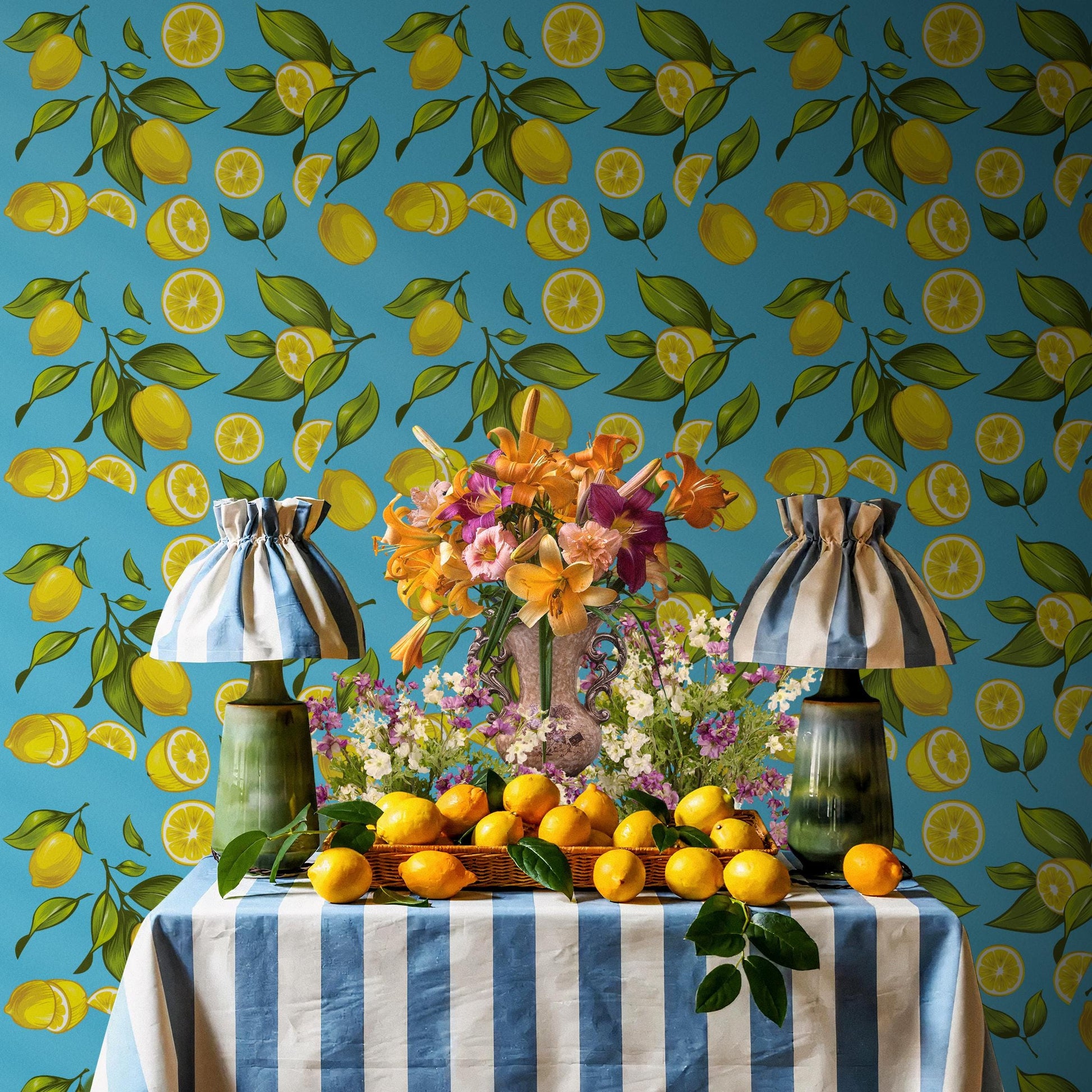 a table with a blue and white striped tablecloth, a vase of flowers, and a basket of oranges. The table is set against a wall with a pattern of yellow and green lemons.