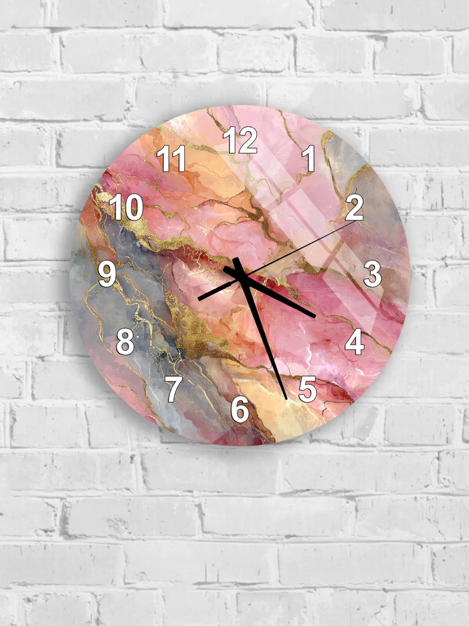 A round wall clock with a pink marble-like design and gold accents, mounted on a white brick wall.