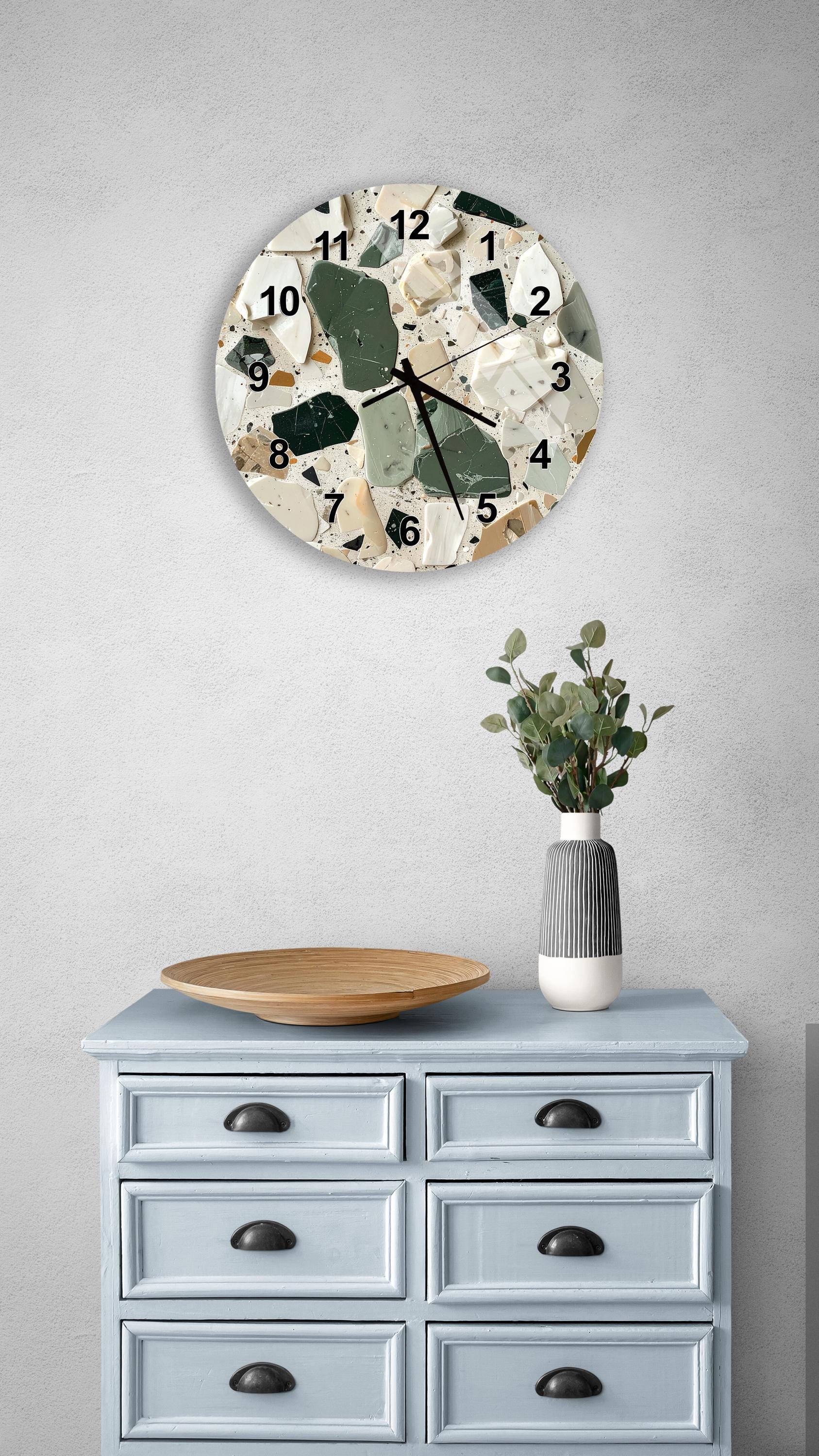 a wall clock with a mosaic design, a wooden tray, a vase with greenery, and a light blue dresser with six drawers.