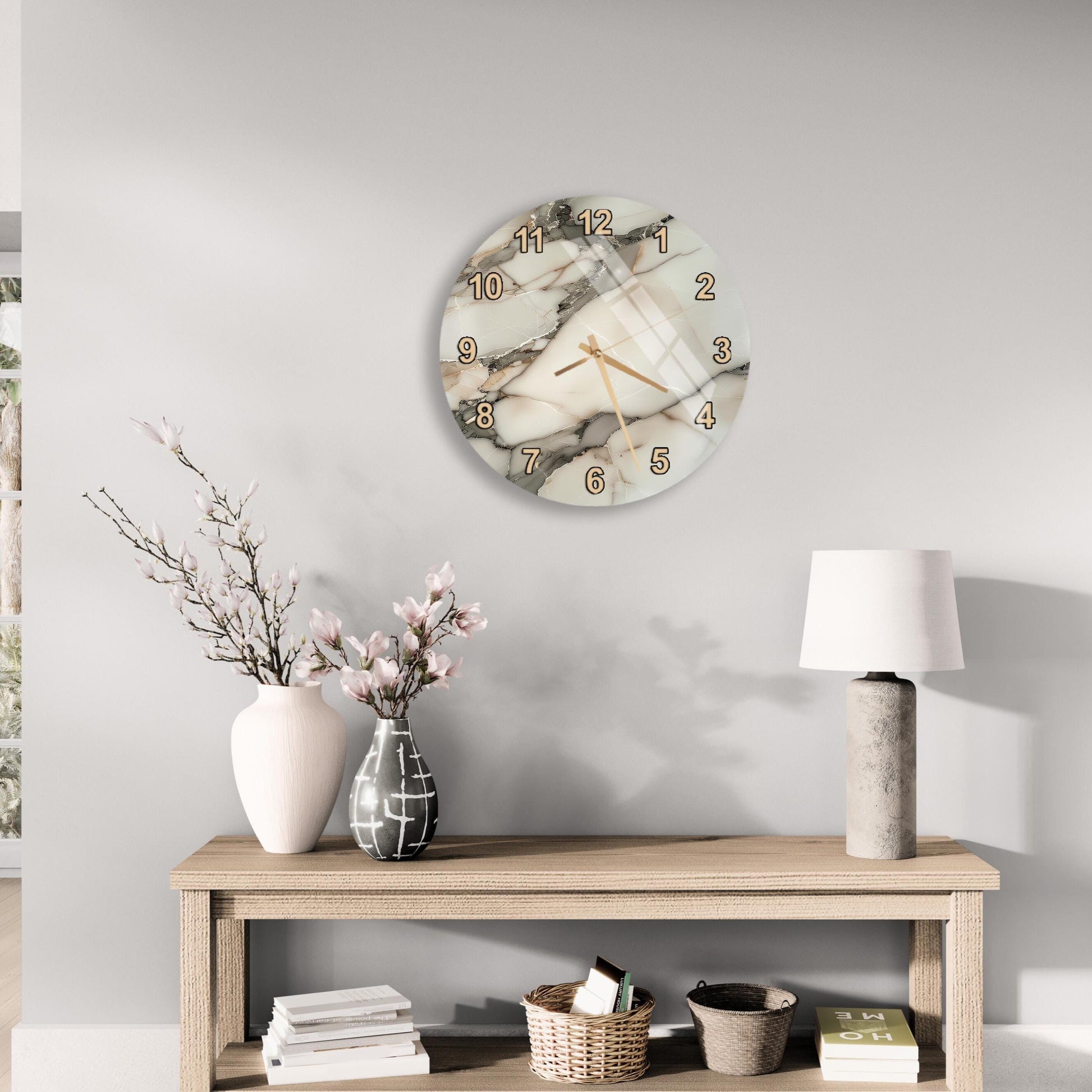 a modern and minimalist living room with a round wall clock, a wooden table with a lamp, a vase with flowers, and a stack of books.
