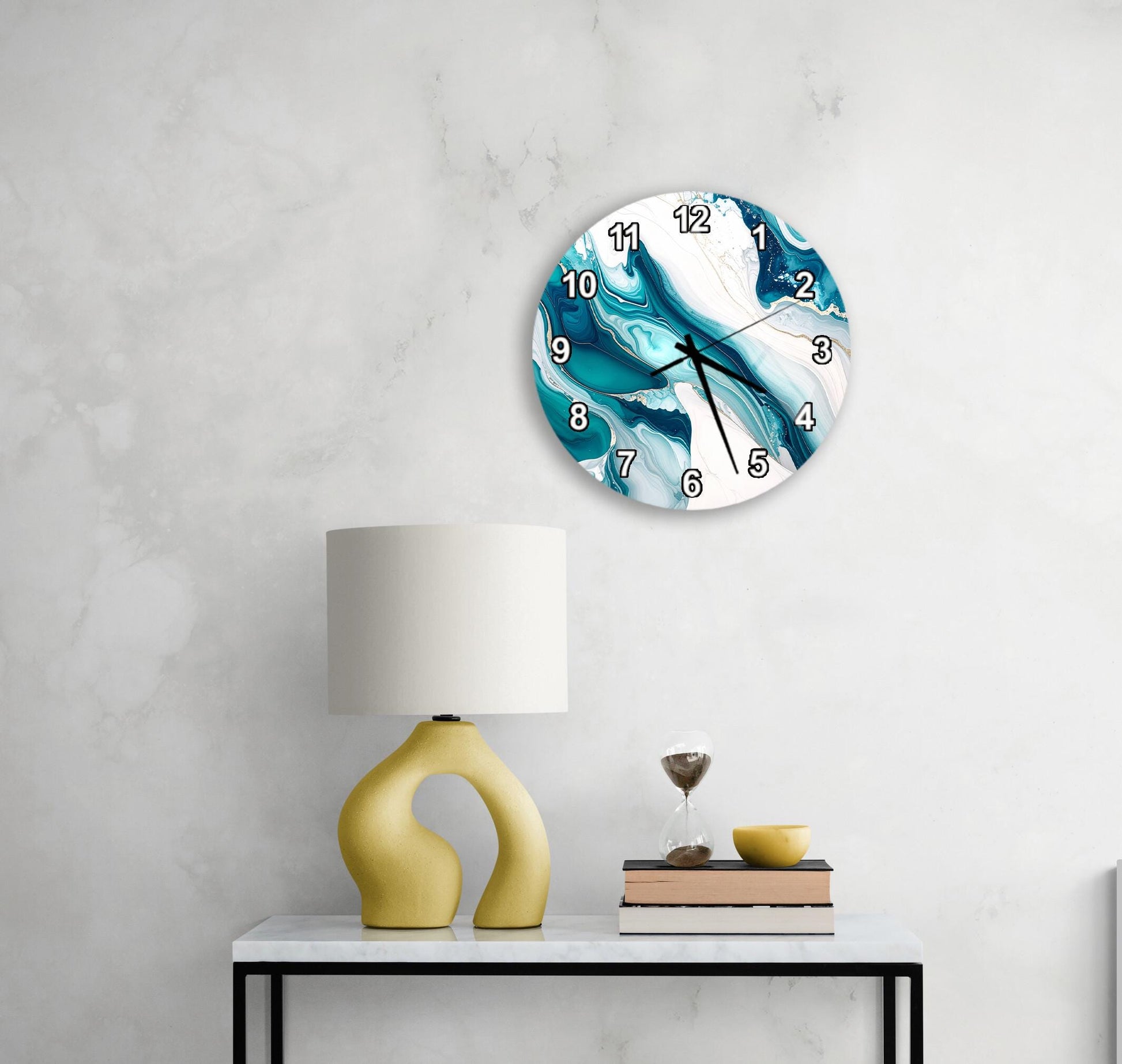 a modern, abstract-style clock with a blue and white swirl design, mounted on a wall above a white table with a yellow lamp and a stack of books.