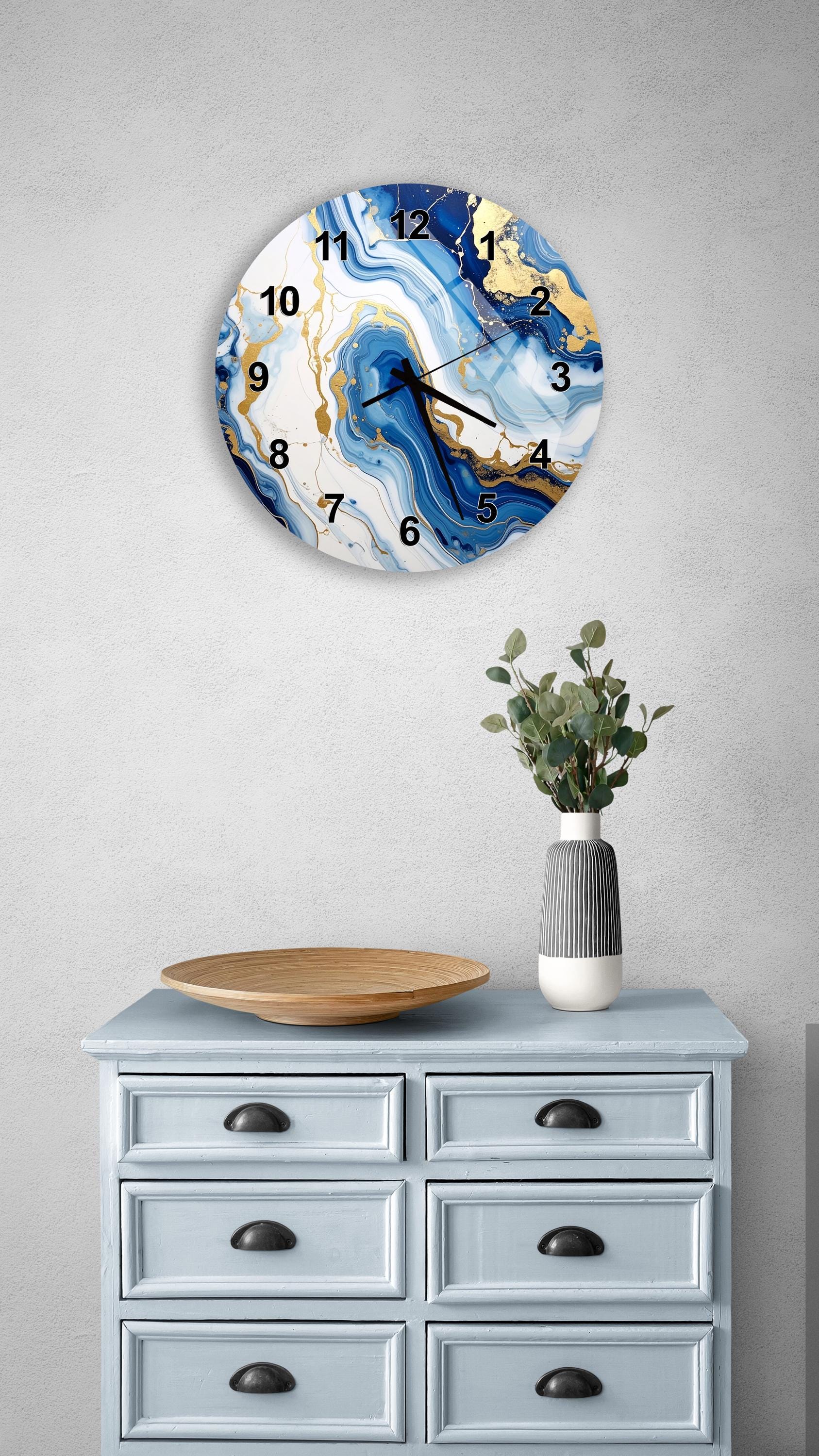a wall clock with a blue and white marble design, mounted on a wall above a light blue dresser with six drawers. The dresser also has a vase with greenery on it, and a wooden tray on top.