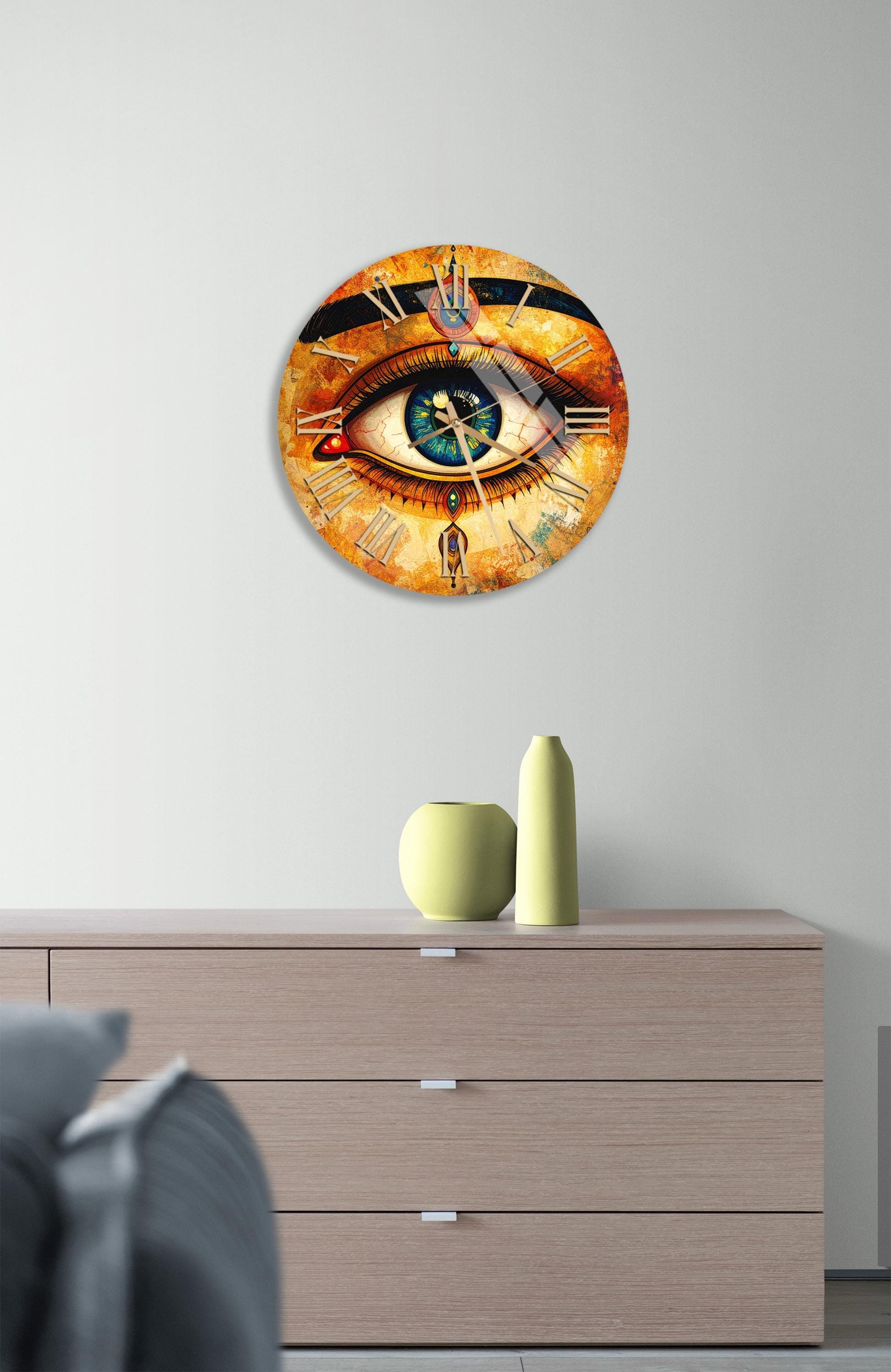 a large, round clock with an eye design on the face, mounted on a wall above a wooden dresser.