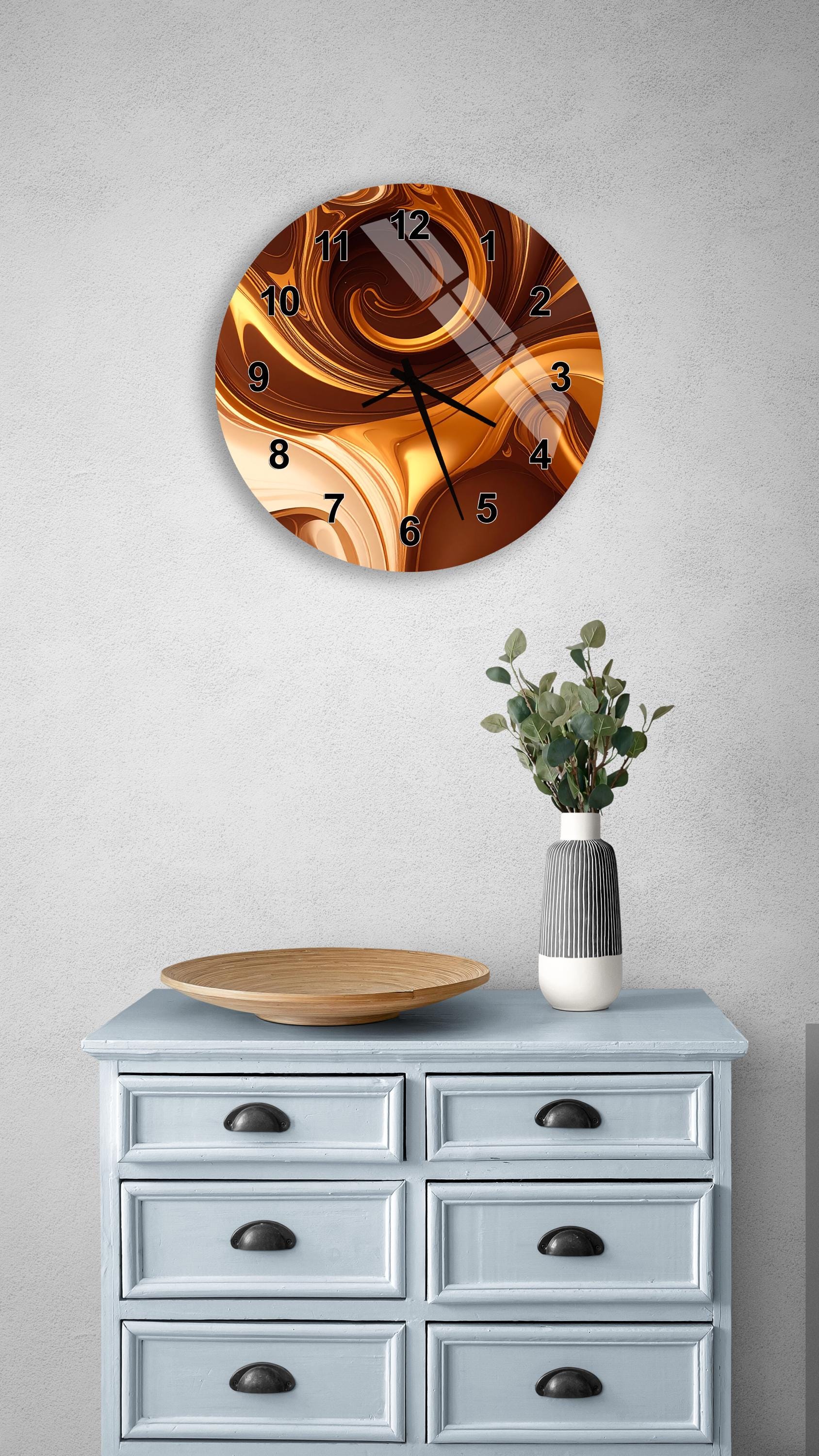 a wall clock with a swirling design, a wooden tray, a vase with greenery, and a gray dresser with six drawers.