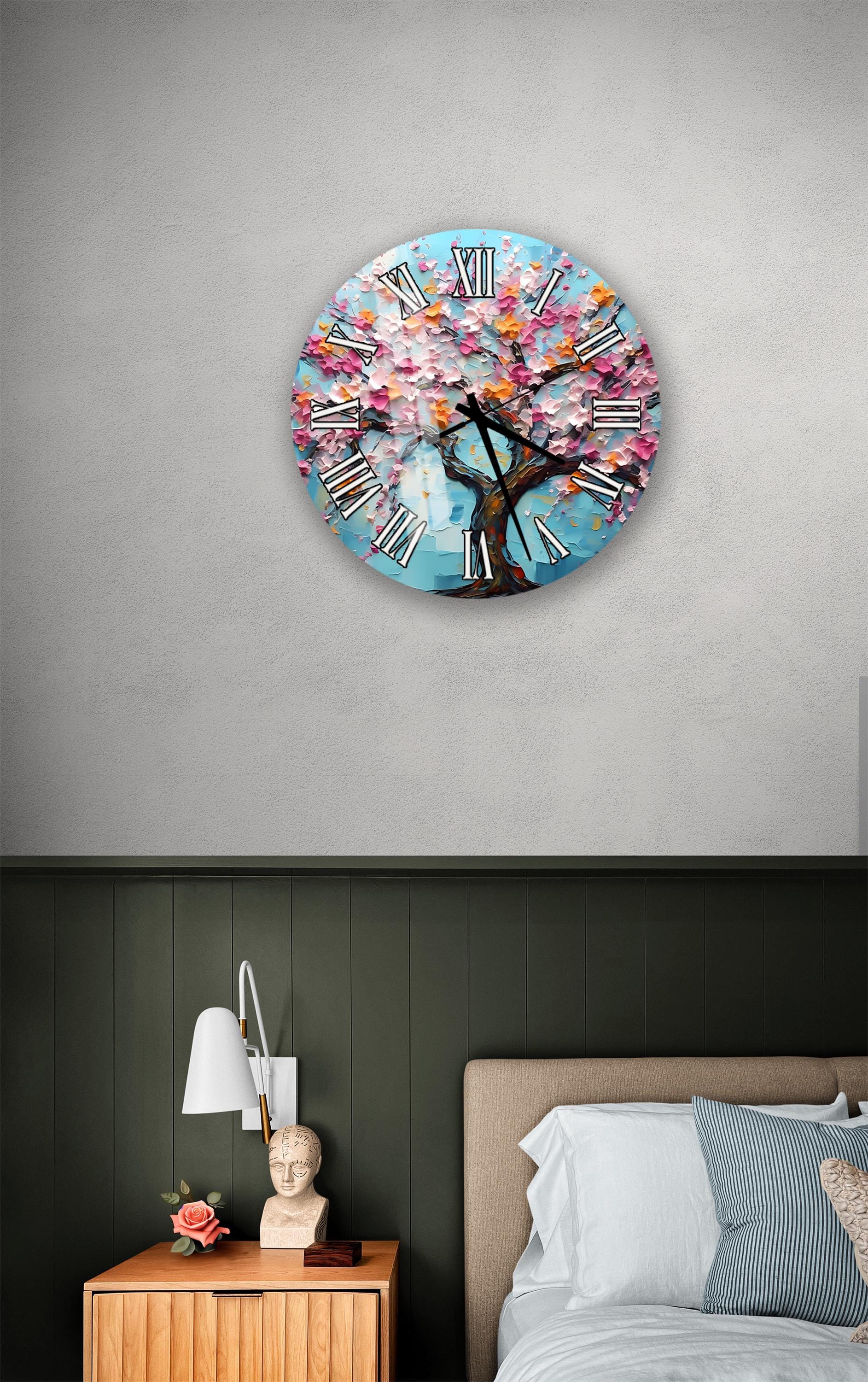 a bedroom setting with a large wall clock displaying a tree with pink flowers, a wooden nightstand with a lamp, and a bed with white pillows.