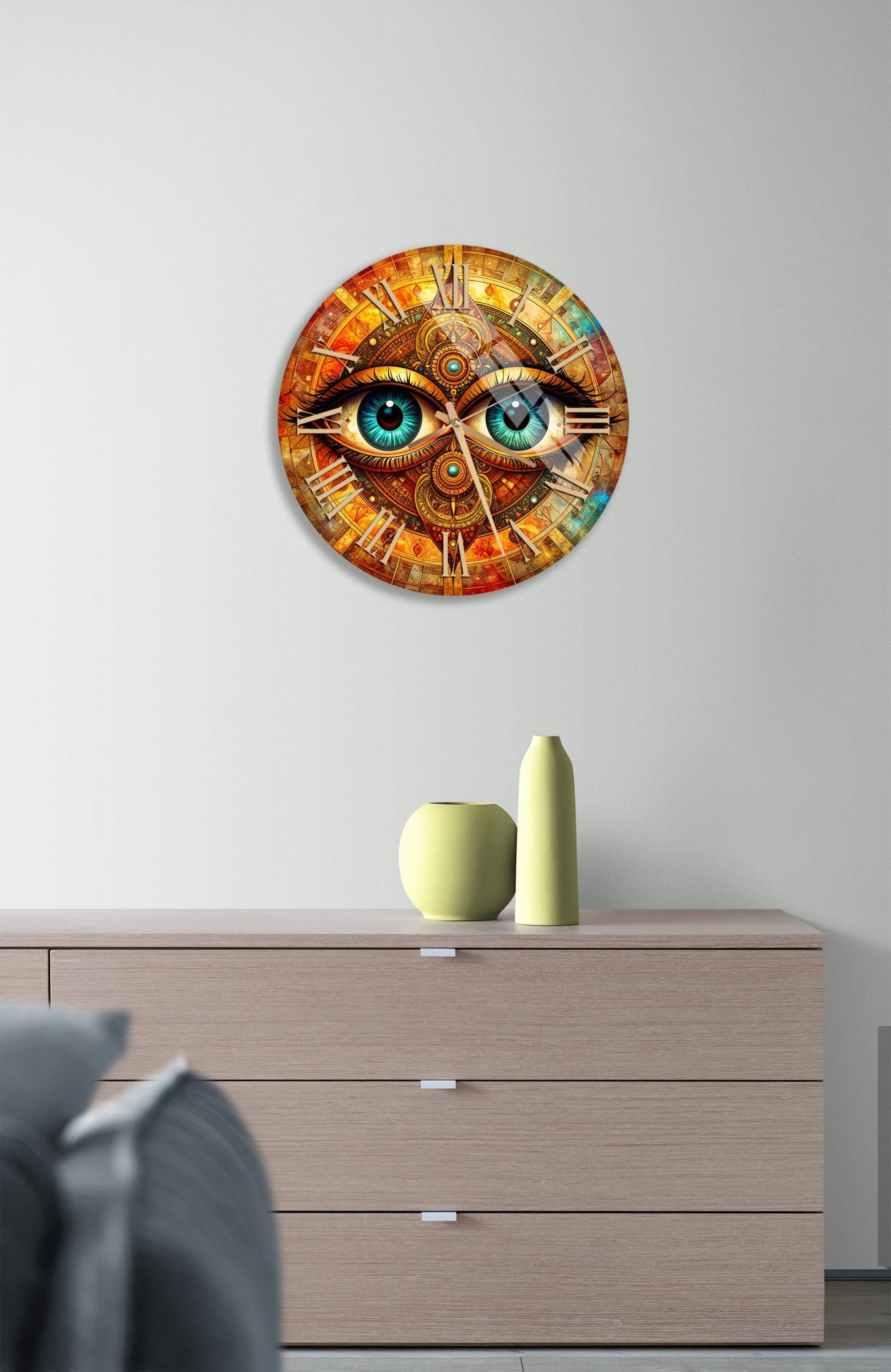 a clock with a unique design, featuring a pair of eyes on the face. The clock is mounted on a wall above a wooden dresser, which has a vase and a small sculpture on it.