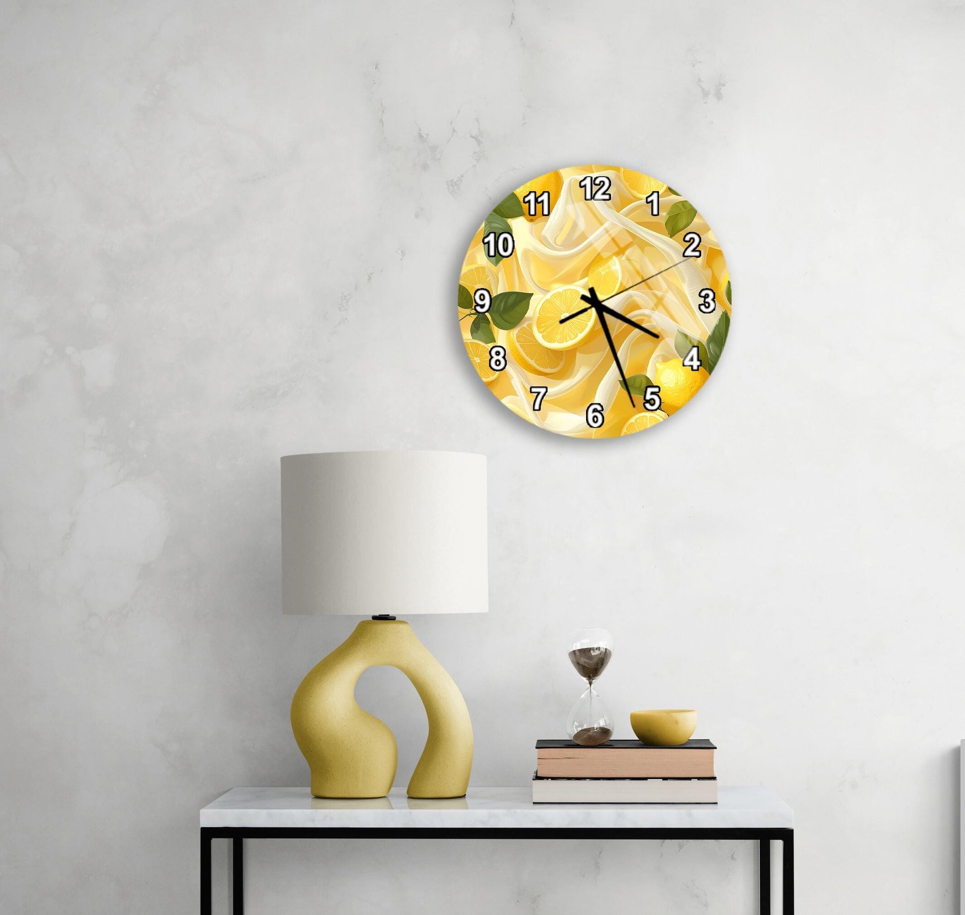 a white wall with a round clock displaying a lemon design, a yellow lamp, a stack of books, and a glass of wine on a white table.
