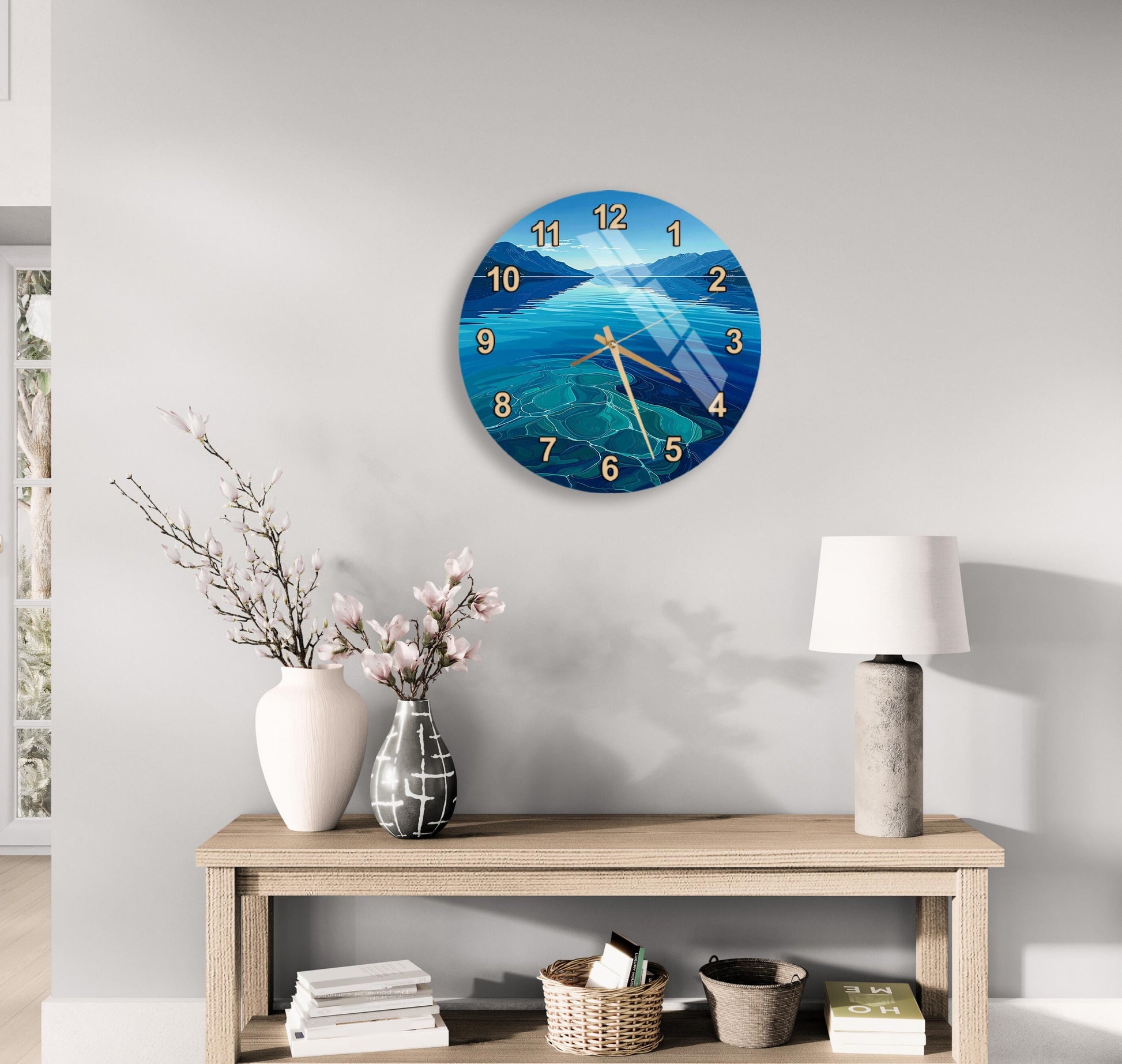 a wall clock with a blue ocean scene, a wooden table with a lamp, a vase with flowers, and some books on a shelf.