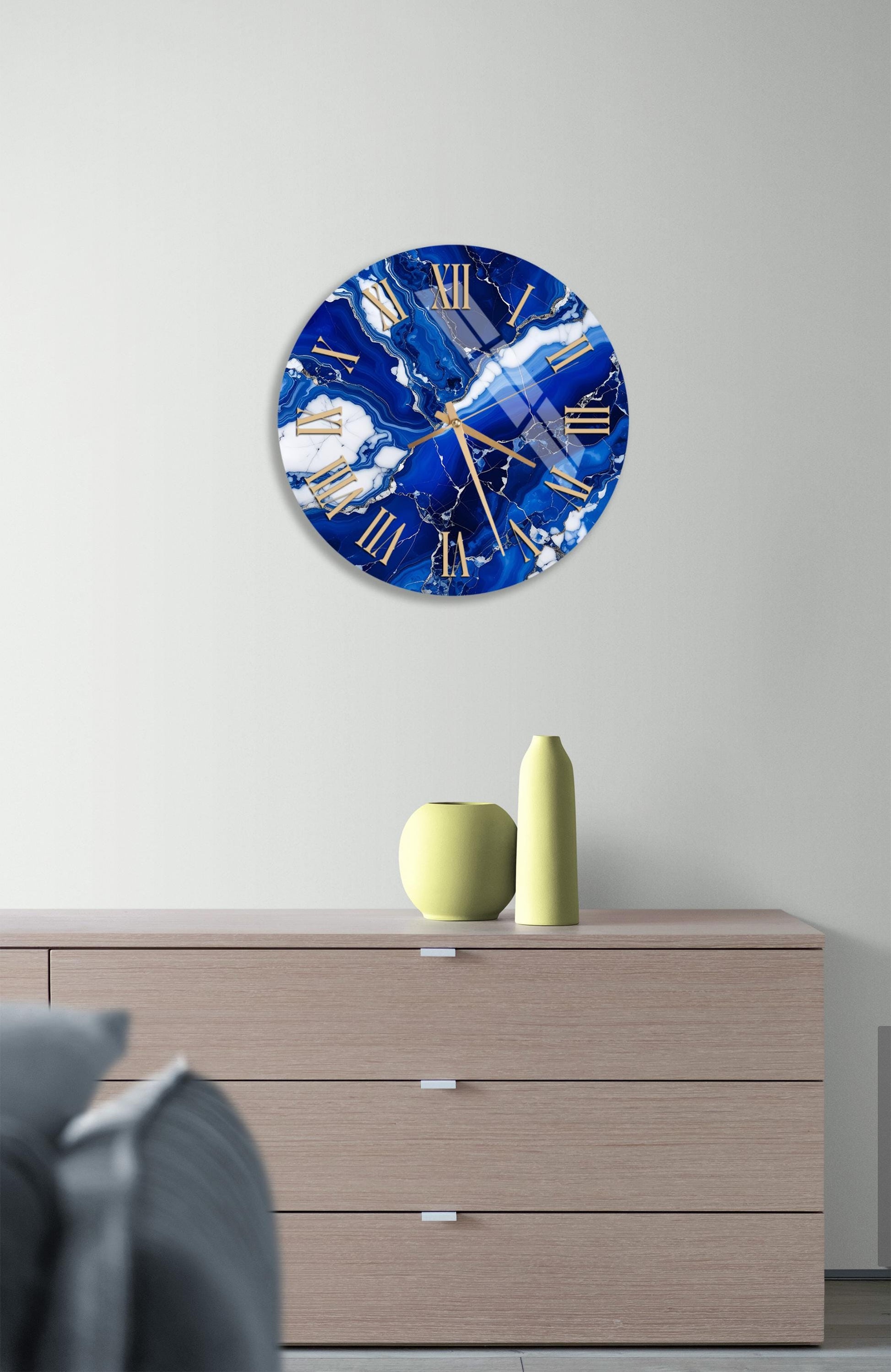 a large blue and white clock with gold hands and numbers, mounted on a wall above a wooden dresser.