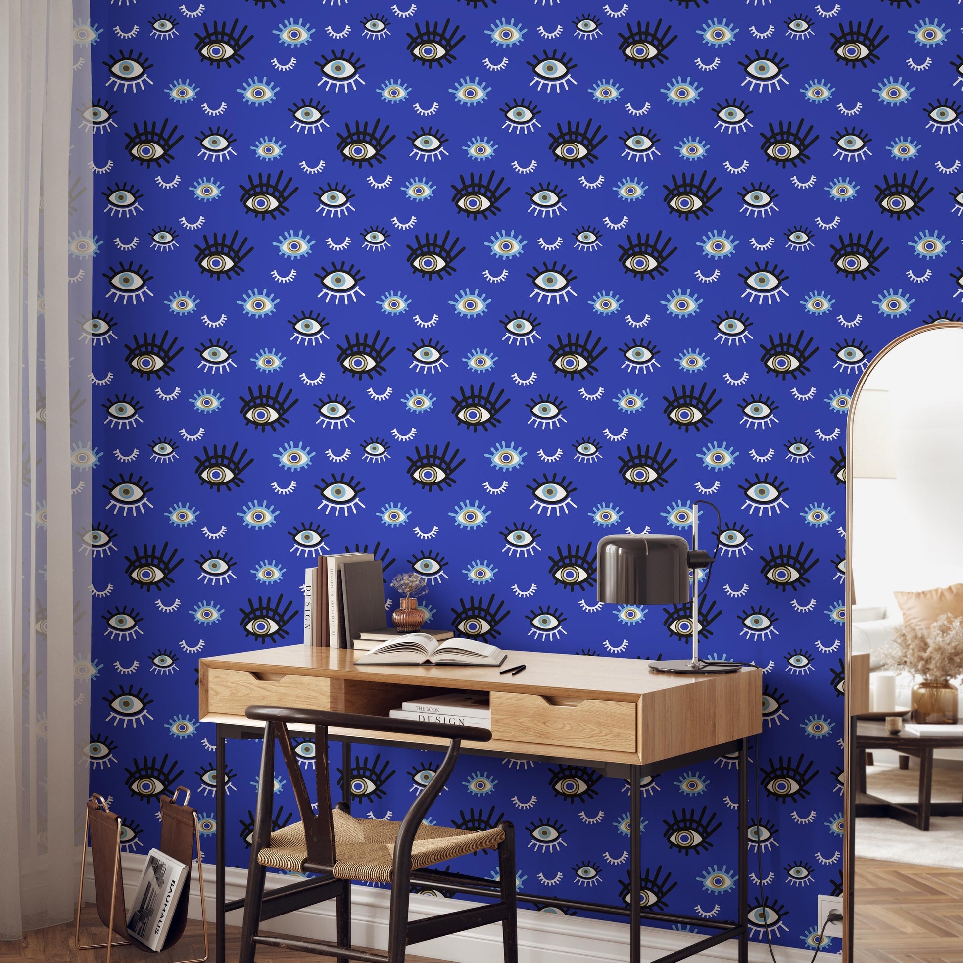 a room with a blue wall adorned with a pattern of large eyes. In the foreground, there is a wooden desk with a lamp and a book, as well as a chair. The room also includes a doorway and a window, suggesting it is part of a larger space.