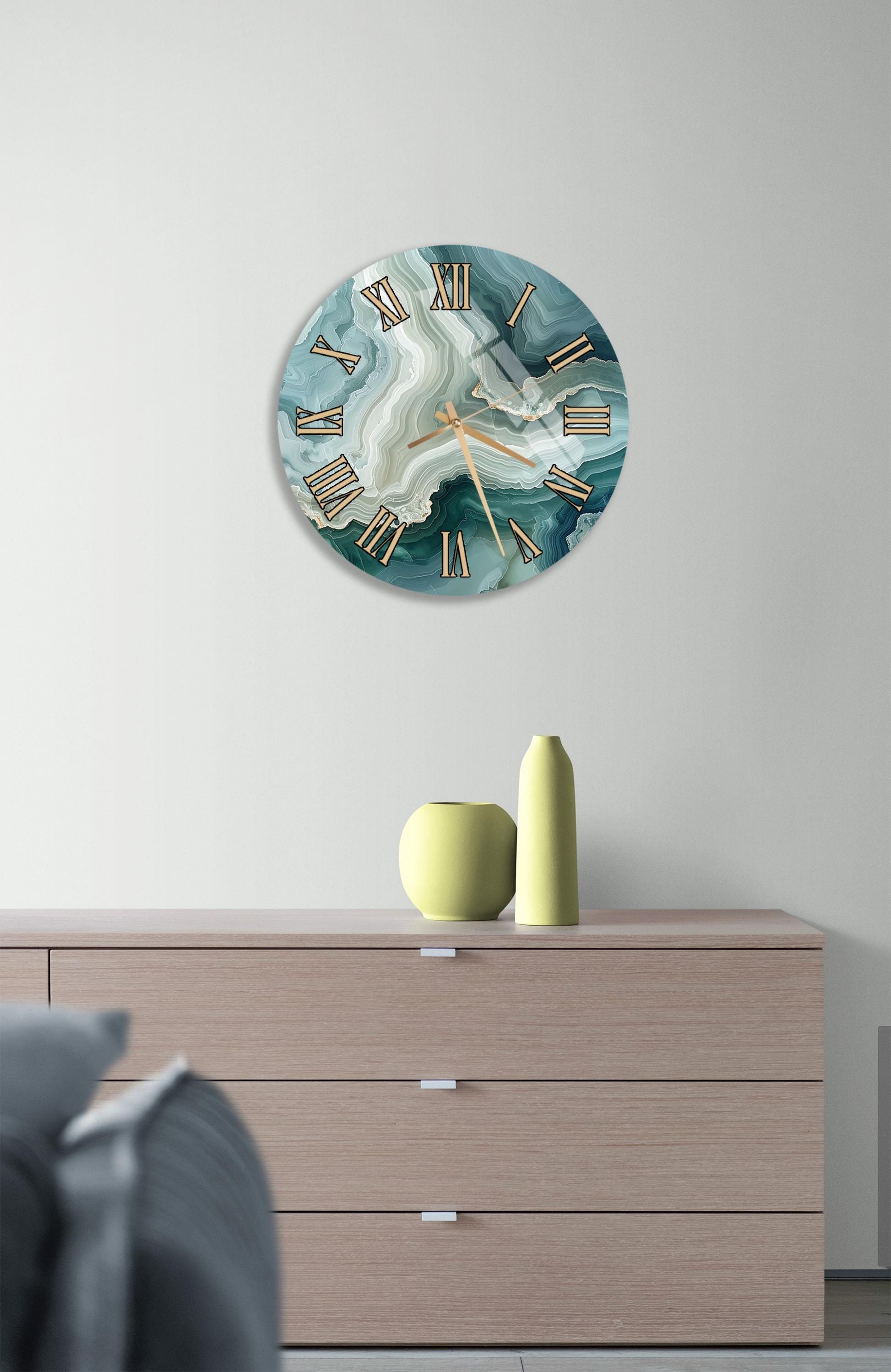 a wall clock with a marble-like design, mounted on a wall above a wooden dresser with three drawers. The dresser also has a small vase and a yellow pot on it.