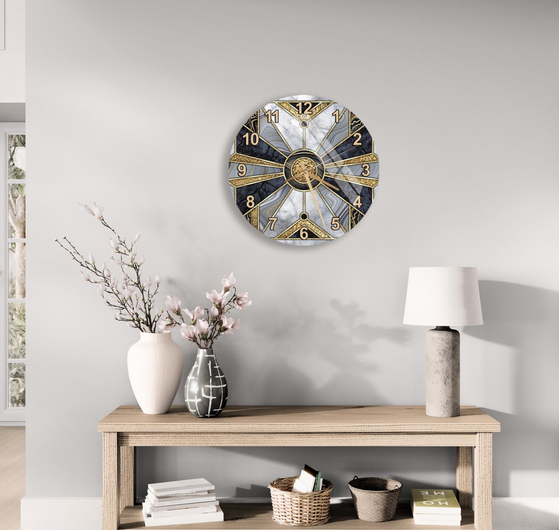 a modern, round clock with a gold and black design, mounted on a wall above a wooden table with a lamp and decorative items.
