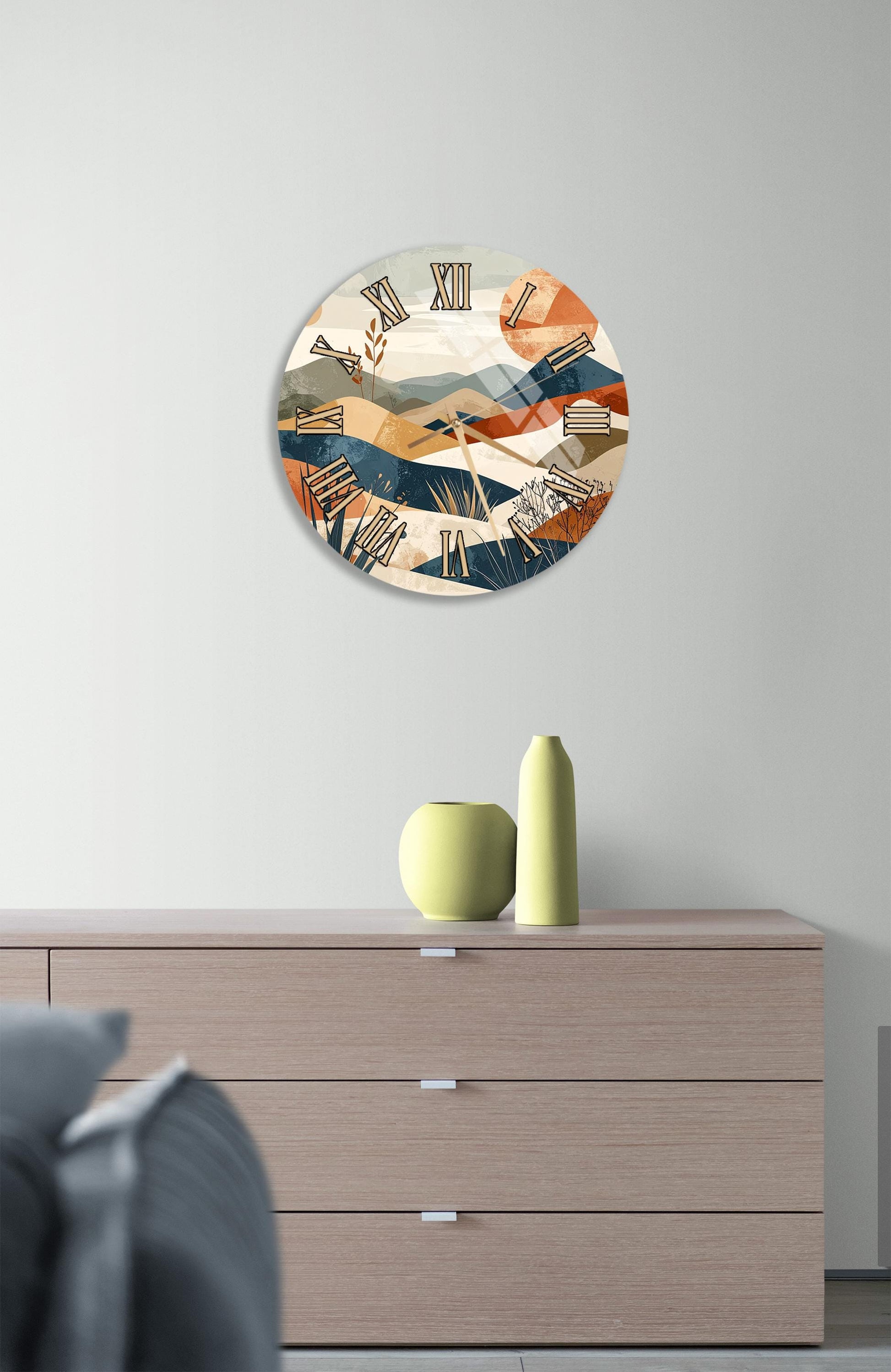 a modern clock with a colorful abstract design, mounted on a wall above a wooden dresser with a vase and a small sculpture on top.