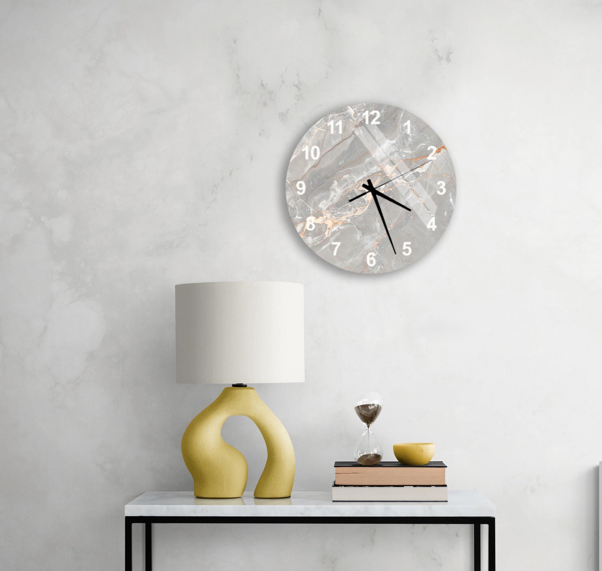 a modern living room with a white marble wall, a round clock with a marble design, a yellow lamp with a unique curved base, a stack of books, and a glass of wine on a white table.